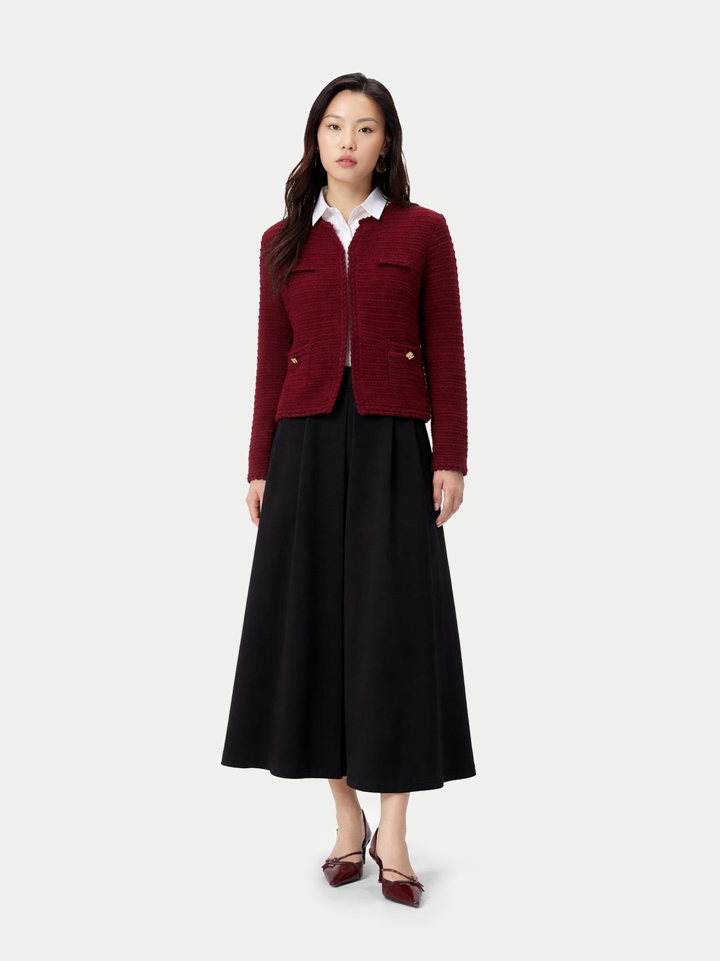 Vue de face d'une femme portant un cardigan bordeaux en maille à col rond et boutons dorés sur les poches latérales, par-dessus une chemise blanche et une jupe noire, sur fond gris clair. #color_Zindanfil