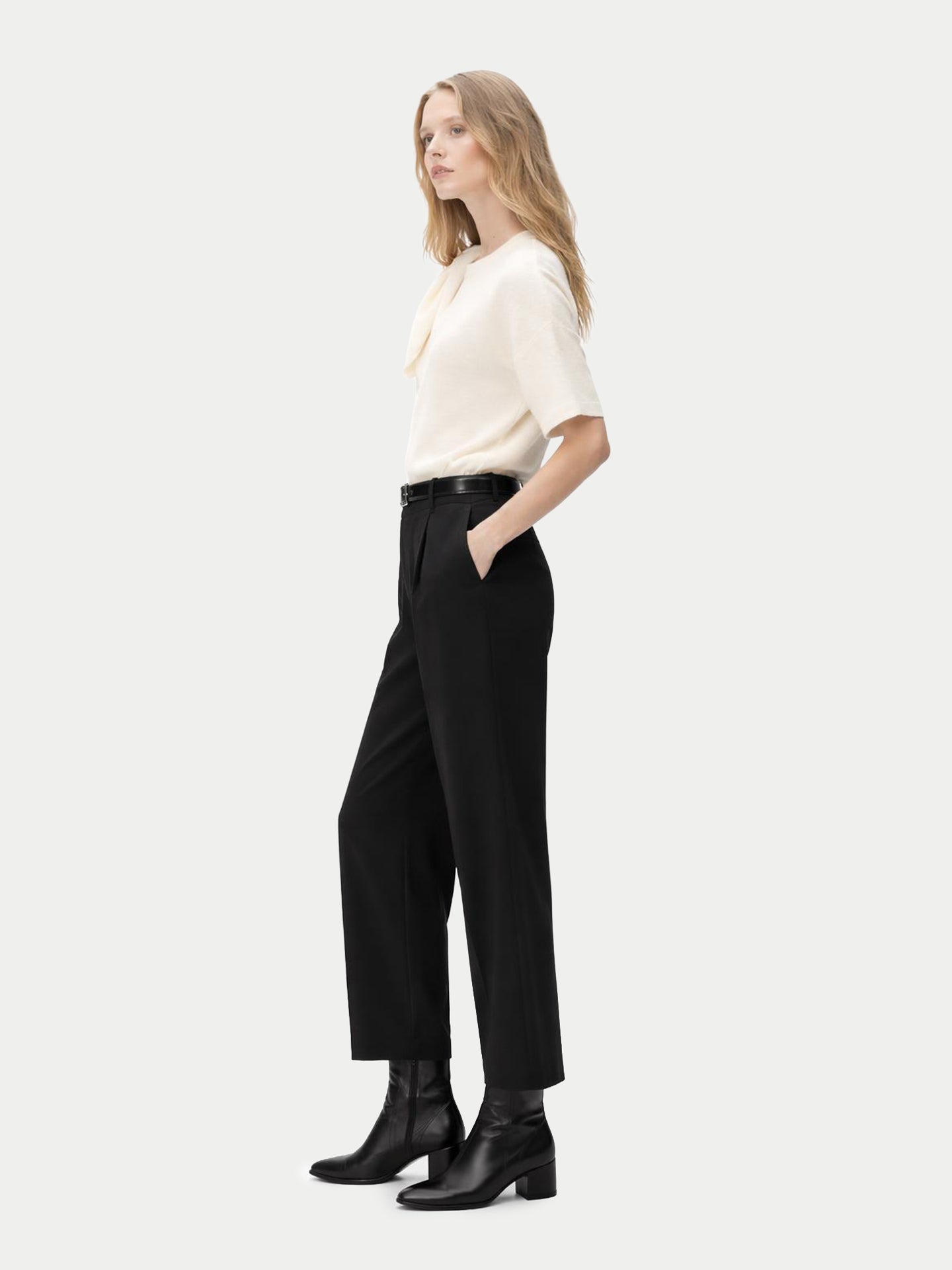Vue de profil d'une femme portant un haut en cachemire blanc à manches courtes et col rond, avec une écharpe nouée sur l'épaule et un pantalon noir, sur fond gris clair. #color_blanc