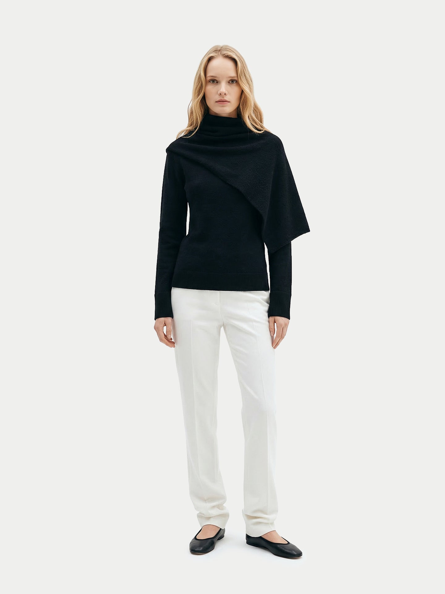 Vue de face d'une femme portant un pull noir à manches longues avec une écharpe intégrée, un pantalon blanc et des ballerines noires sur un fond gris clair.  #color_noir