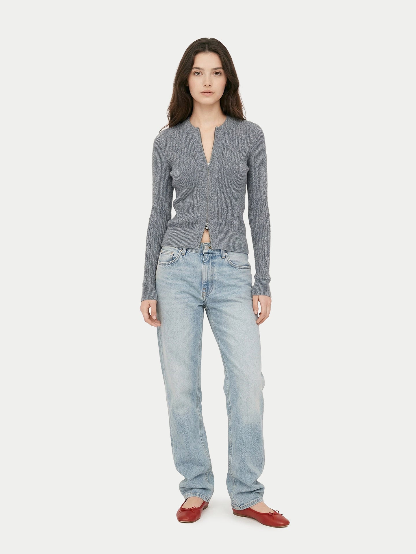 Vue de face d'une femme portant un cardigan gris à fermeture éclair et col rond côtelé, un jean et des ballerines rouges sur un fond gris clair. #color_gris-pierre