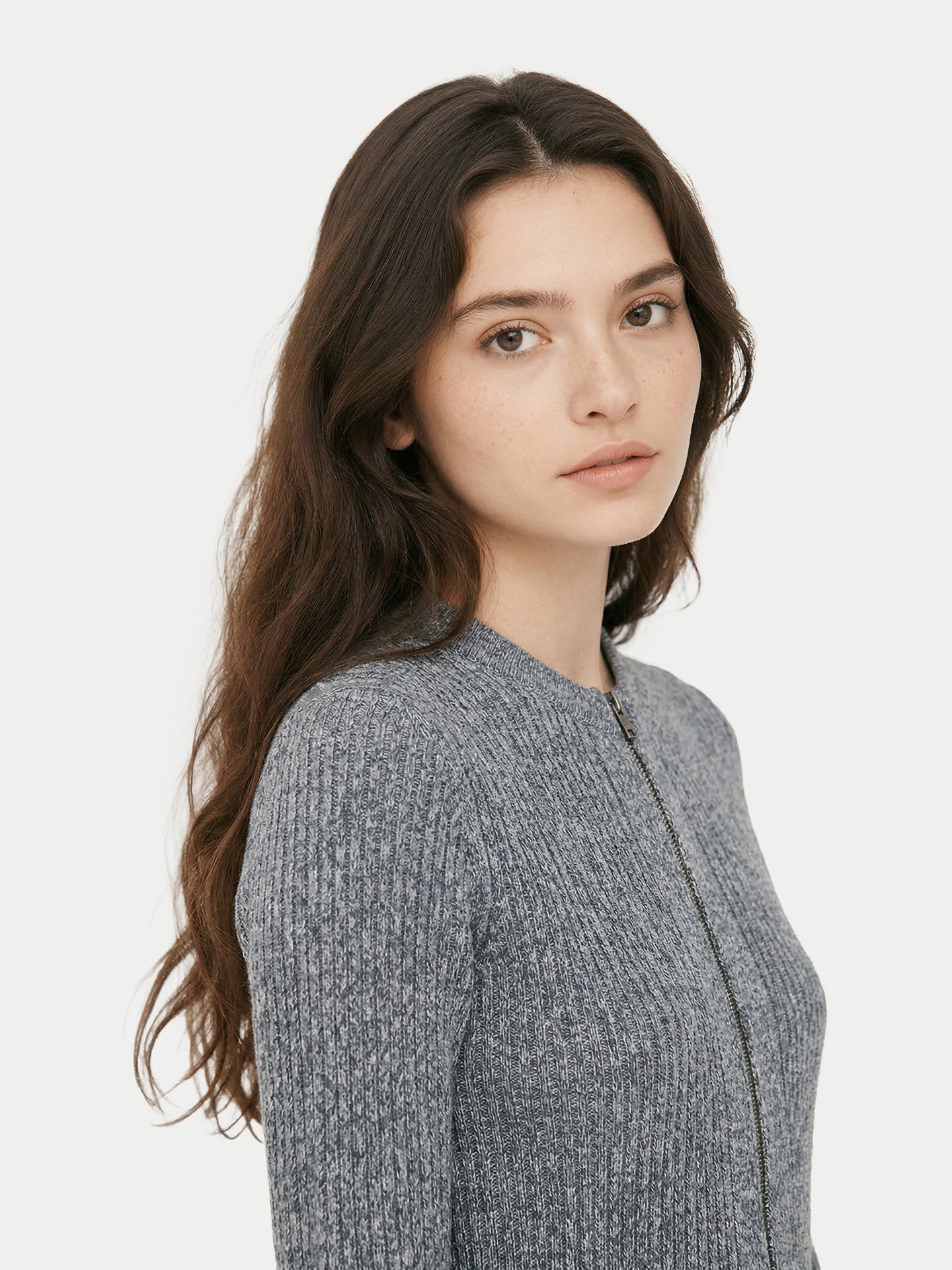 Gros plan de profil d'une femme portant un cardigan gris côtelé à fermeture éclair et col rond sur un fond gris clair. #color_gris-pierre