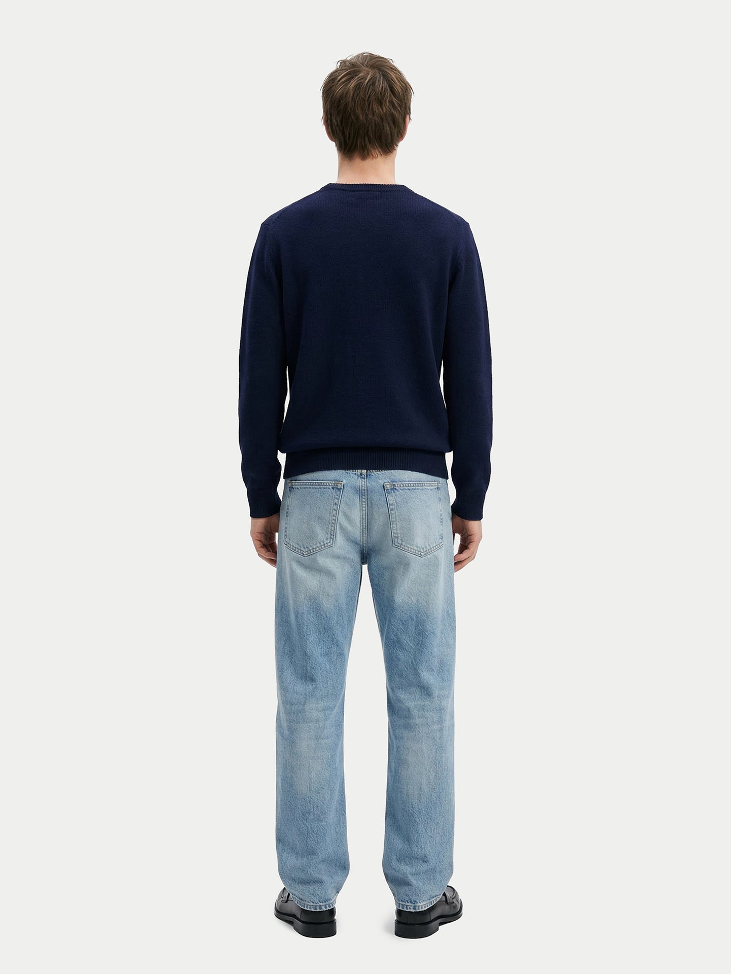Vue de dos d'un homme portant un pull bleu marine et un jean bleu sur fond gris clair. #color_navy