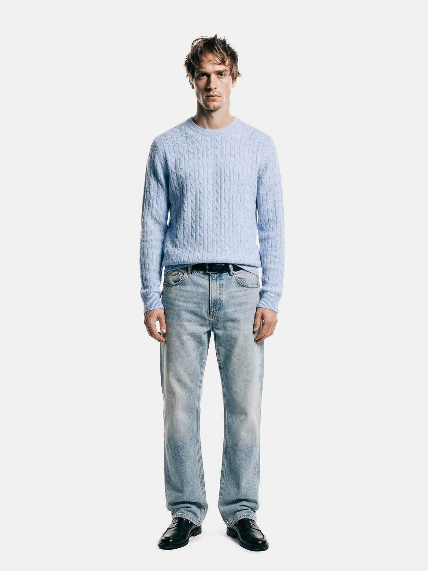 Vue de face d'un homme portant un pull en maille torsadée bleu clair et un jean sur fond gris clair. #color_bleu-clair