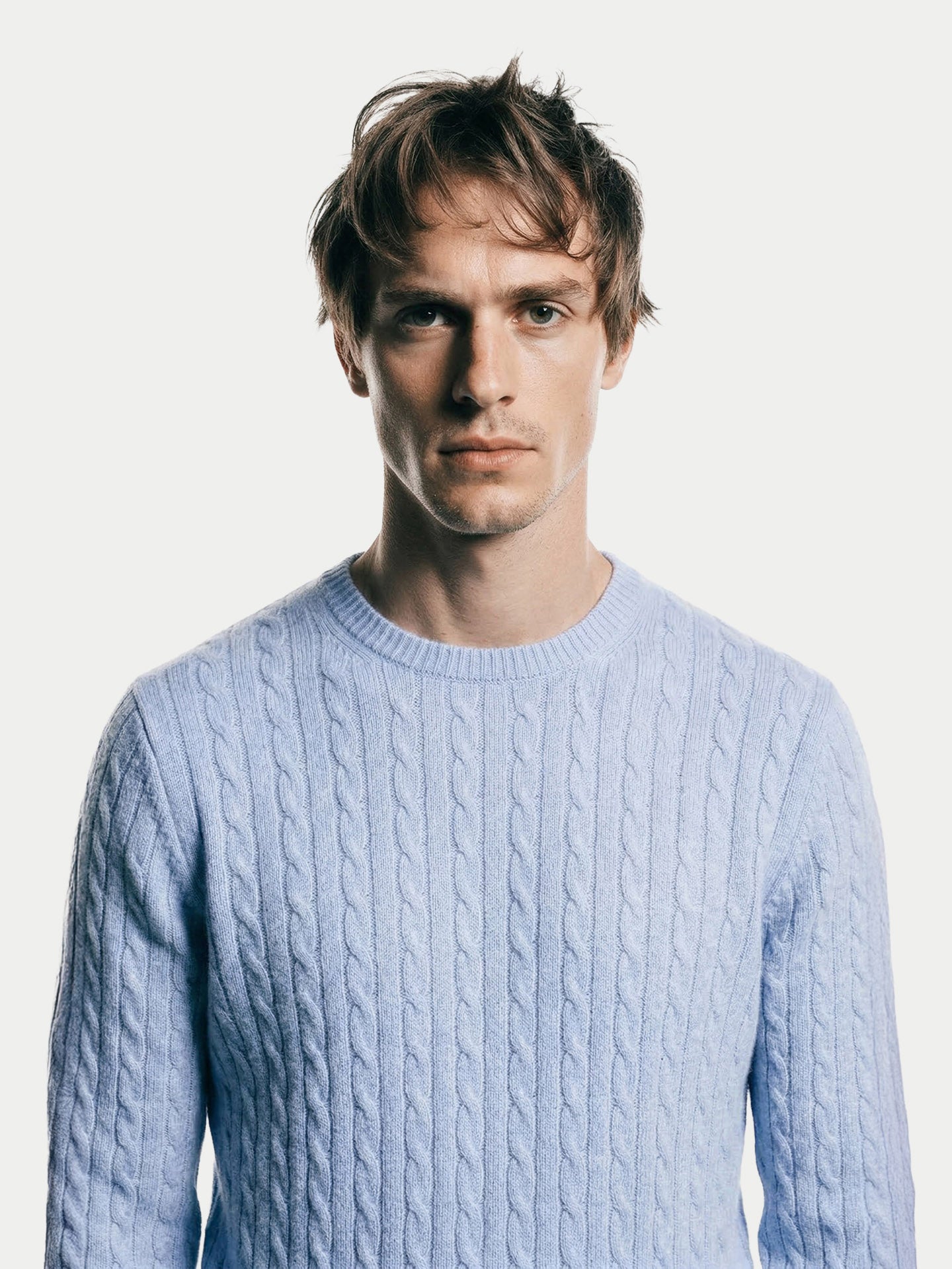 Gros plan de face d'un homme portant un pull en maille torsadée bleu clair sur fond gris clair. #color_bleu-clair