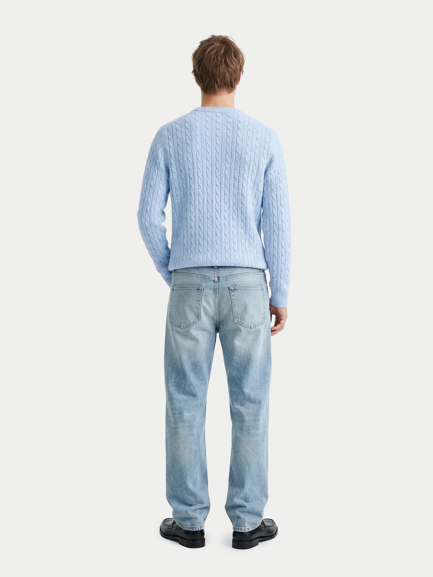 Vue de dos d'un homme portant un pull en maille torsadée bleu clair et un jean bleu sur fond gris clair. #color_bleu-clair