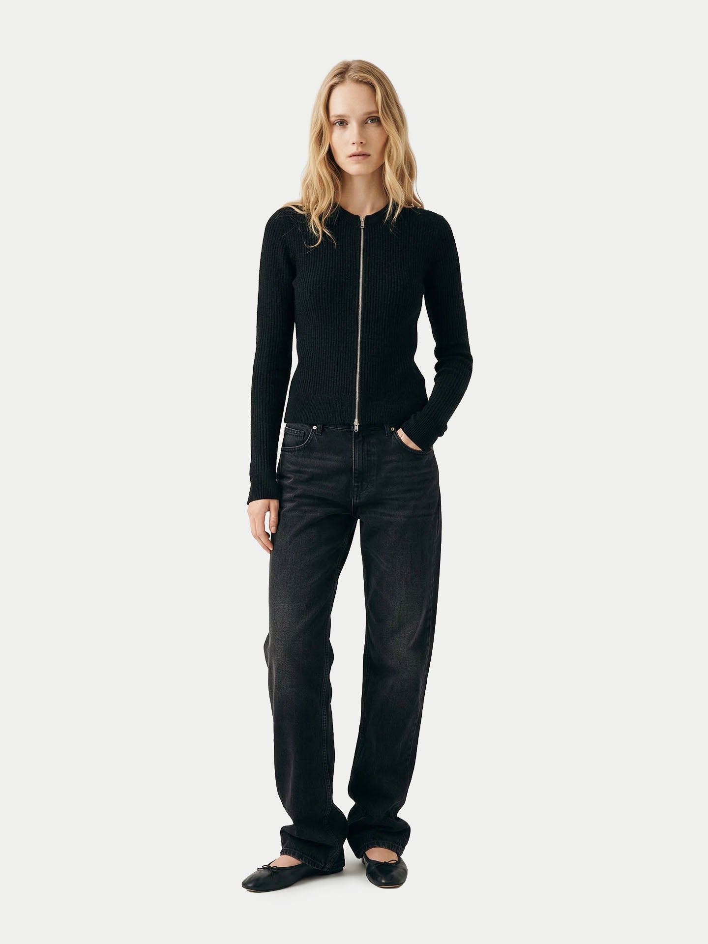 Vue de face d'une femme portant un cardigan noir à fermeture éclair et col rond côtelé assorti à un pantalon, sur un fond gris clair. #color_noir