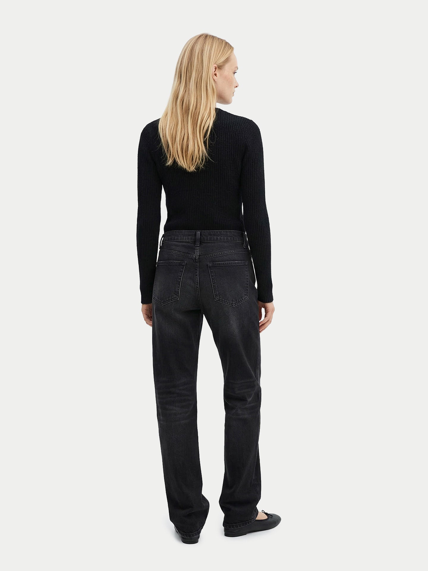 Vue de dos d'une femme portant un cardigan noir côtelé assorti à un pantalon, sur un fond gris clair. #color_noir