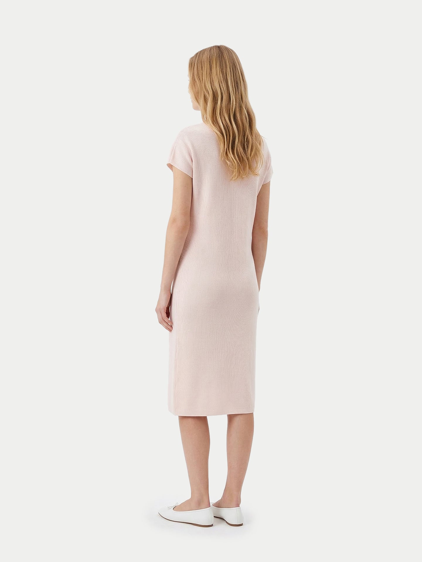 Vue de dos d'une femme portant une robe rose arrivant sous le genou et des ballerines blanches sur un fond gris clair. #color_peach-blush