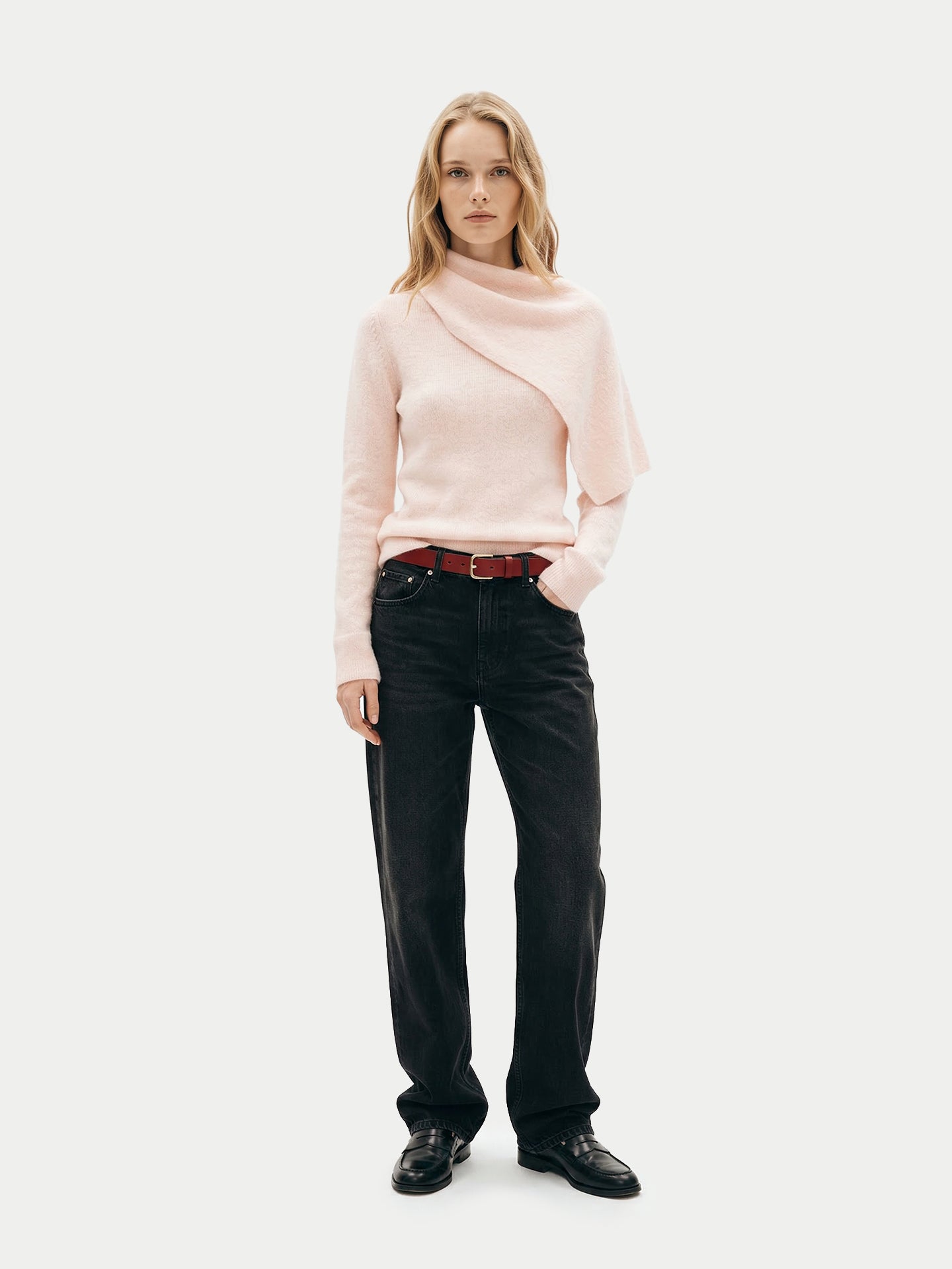 Vue de face d'une femme debout portant un pull rose avec une écharpe intégrée, un jean noir et des mocassins noirs sur un fond gris clair. #color_peach-blush