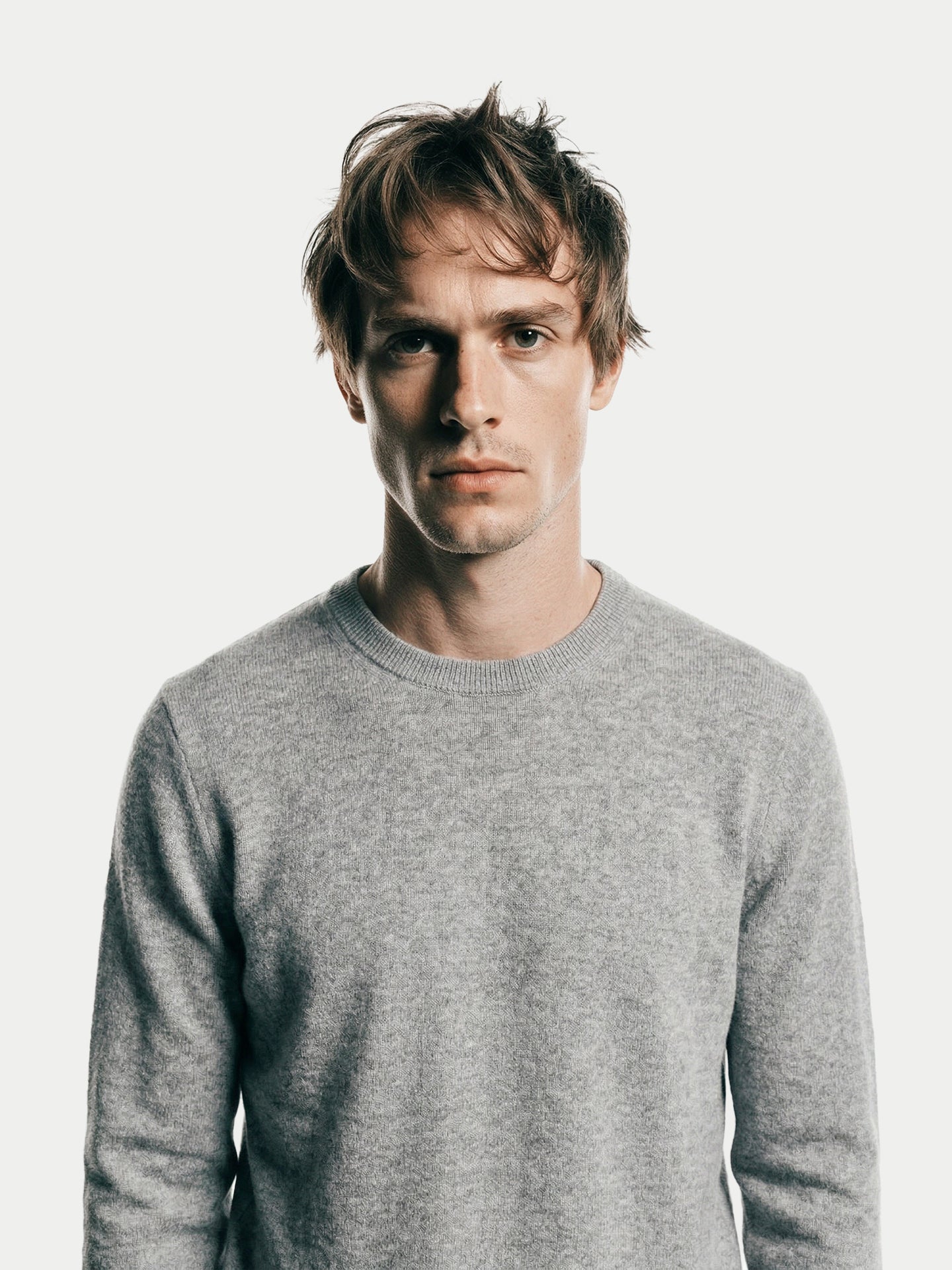 Gros plan de face d'un homme portant un pull gris à col rond et un jean sur fond gris clair. #color_high-rise