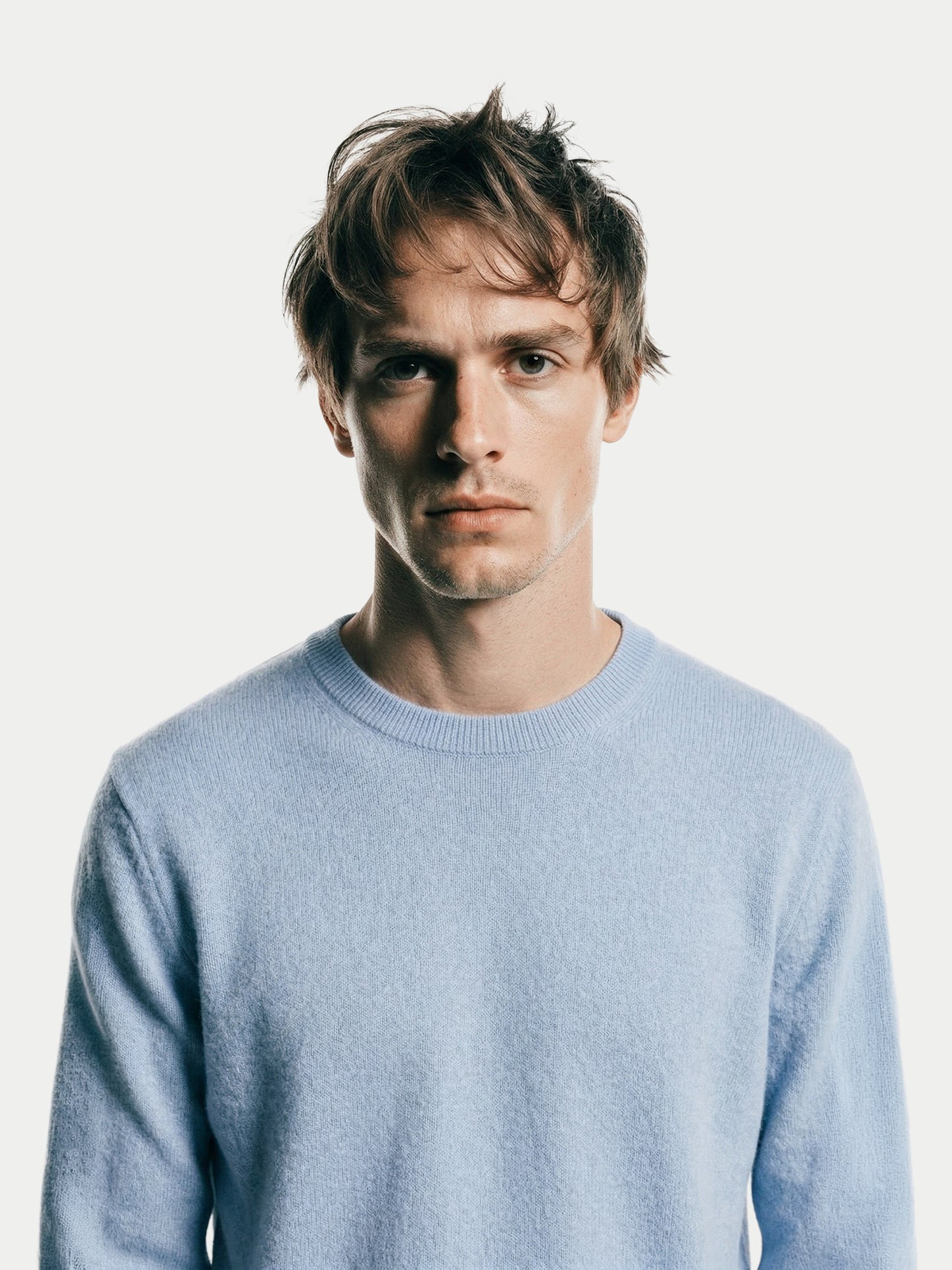 Gros plan de face d'un homme portant un pull bleu clair à col rond sur fond gris clair. #color_bleu-clair