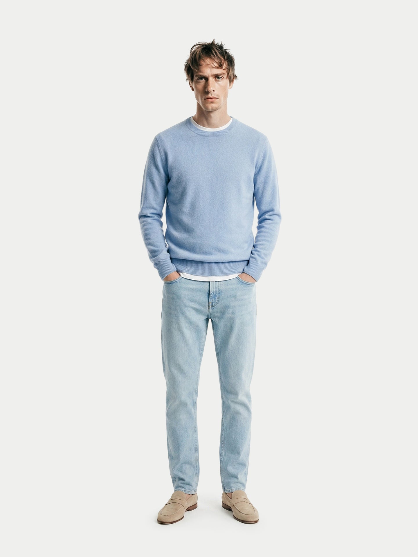 Vue de face d'un homme portant un pull bleu clair à col rond, un jean et des mocassins beiges en cachemire, sur fond gris clair. #color_bleu-clair