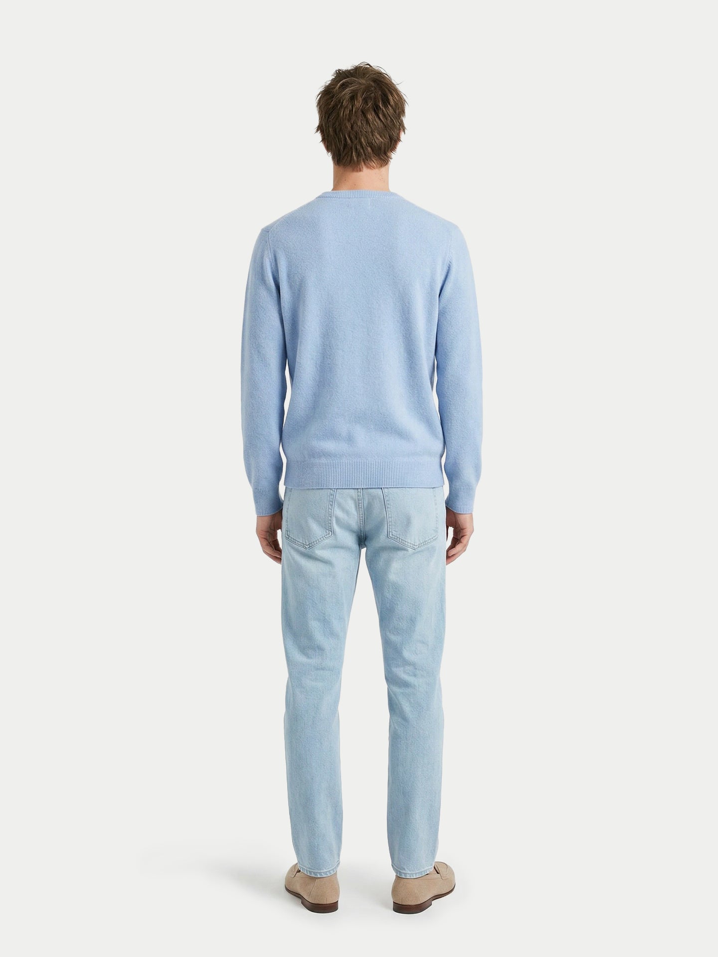 Vue de dos d'un homme portant un pull bleu clair à col rond et un jean sur fond gris clair. #color_bleu-clair