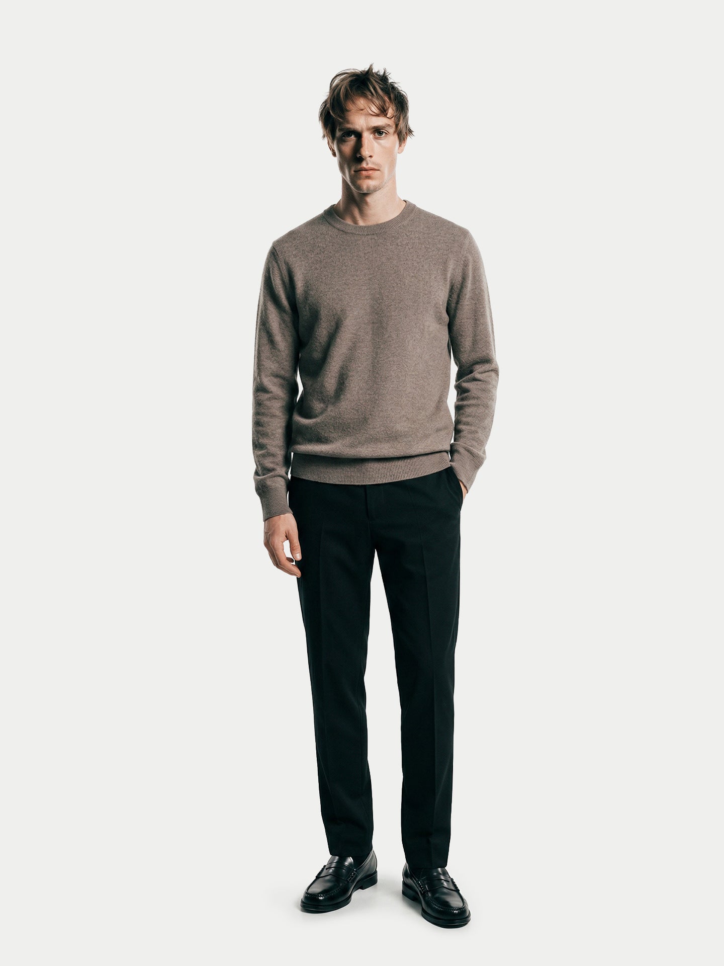 Vue de face d'un homme portant un pull ras du cou taupe et un pantalon noir sur fond gris clair. #color_taupe
