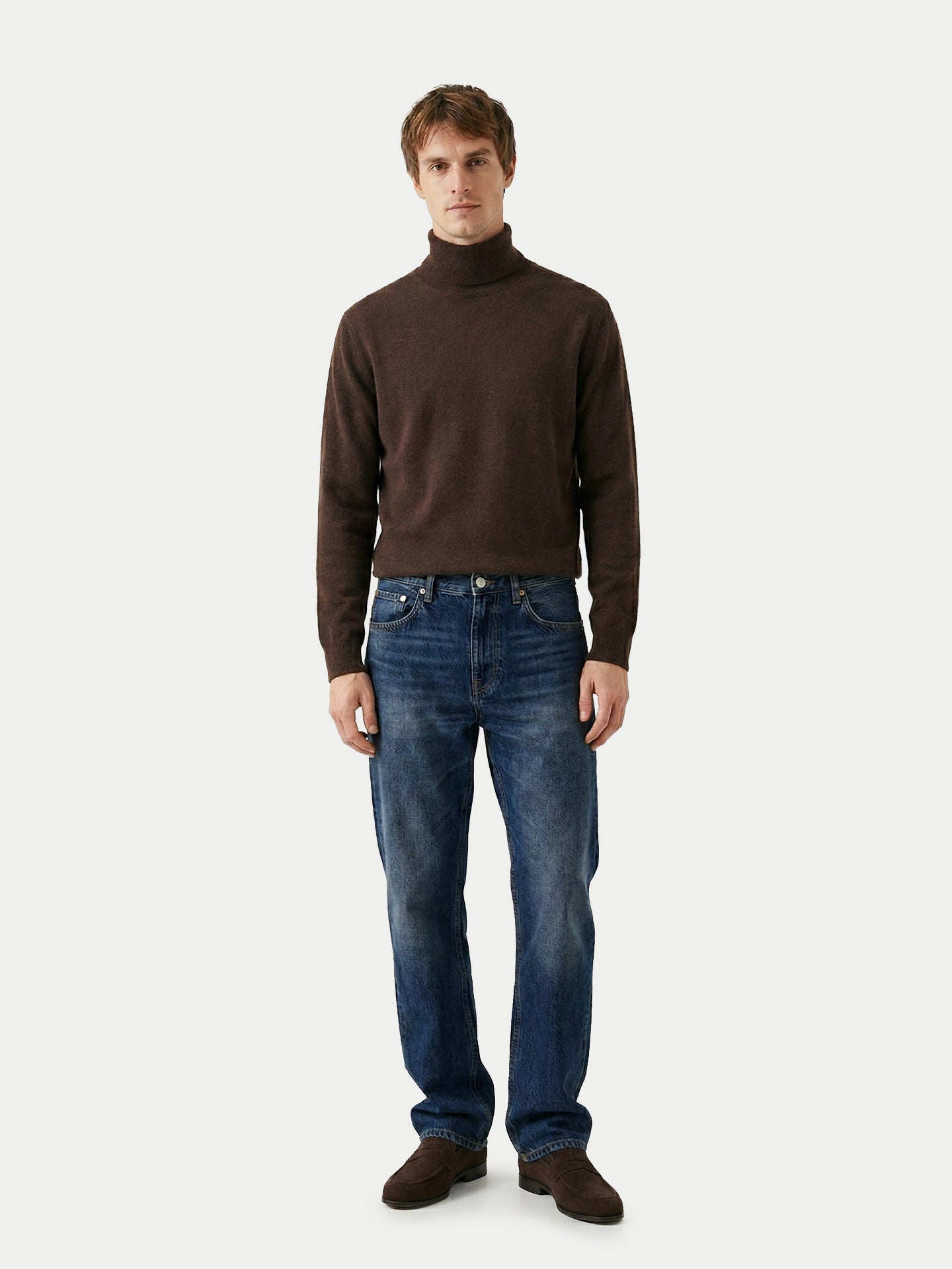 Vue de face d'un homme portant un pull à col roulé marron et un jean bleu sur fond gris clair. #color_cacao