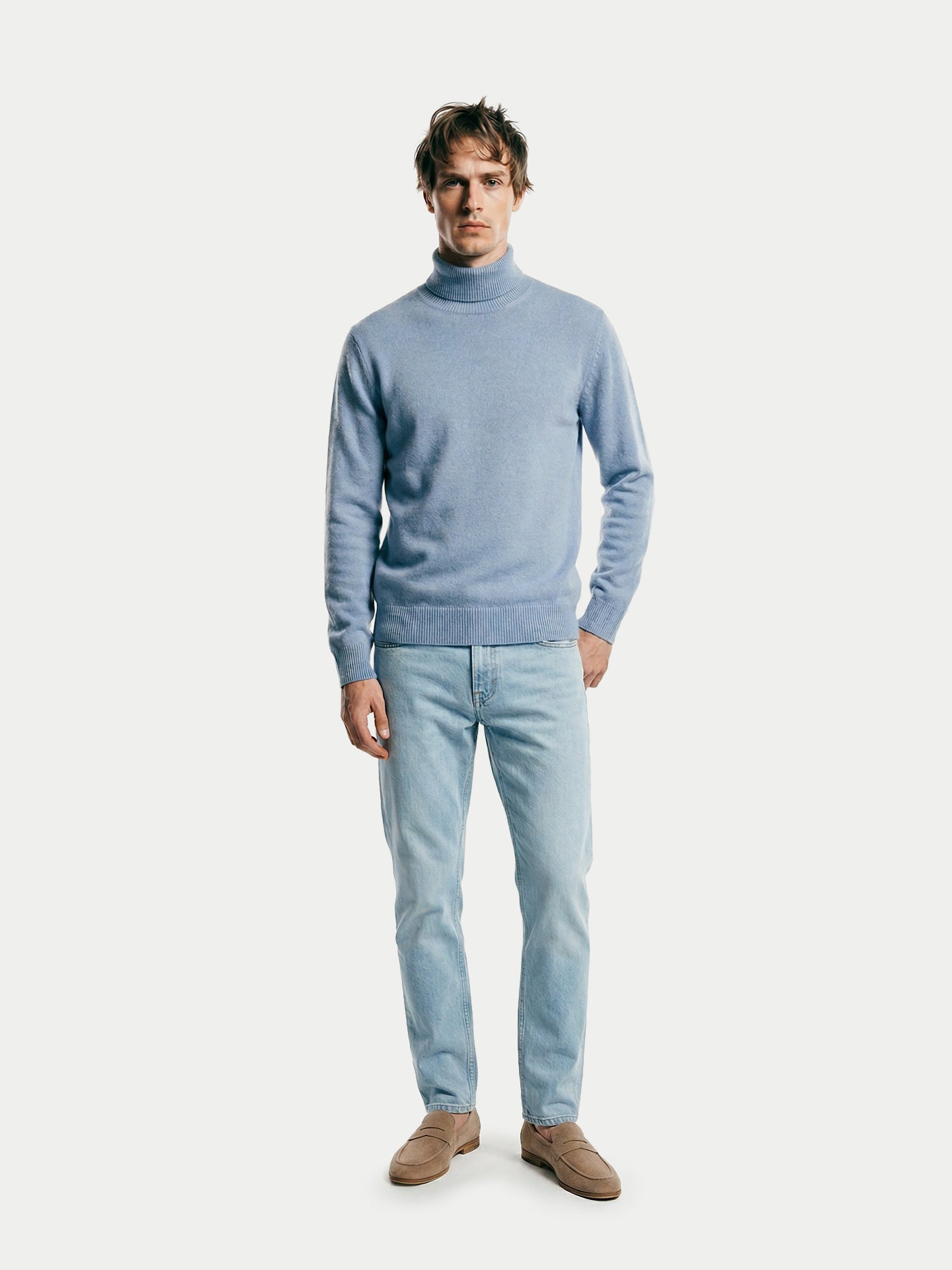 Vue de face d'un homme portant un pull à col roulé bleu clair et un jean sur fond gris clair. #color_bleu-clair