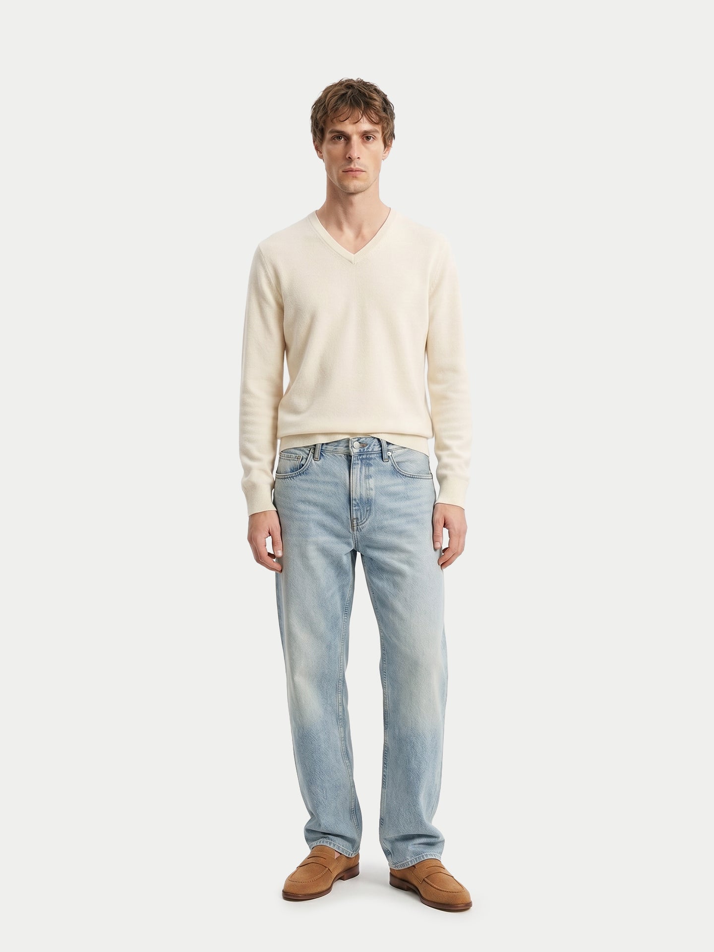 Vue de face d'un homme portant un pull blanc à col en V, un jean bleu et des mocassins marron sur fond gris clair. #color_blanc-cassé