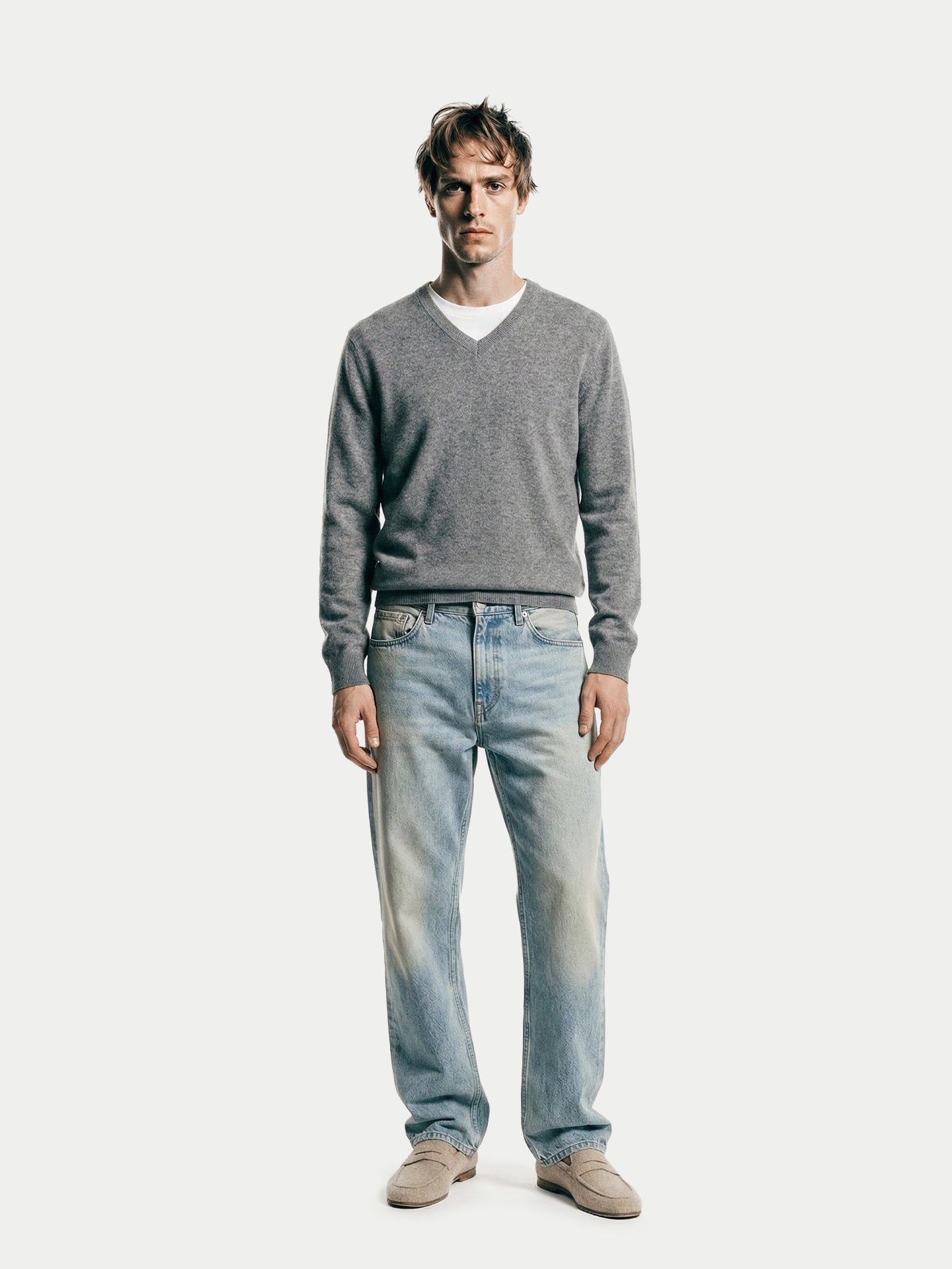 Vue de face d'un pull gris à col en V porté sur un t-shirt blanc, un jean bleu et des mocassins beiges, sur fond gris clair. #color_gris-foncé
