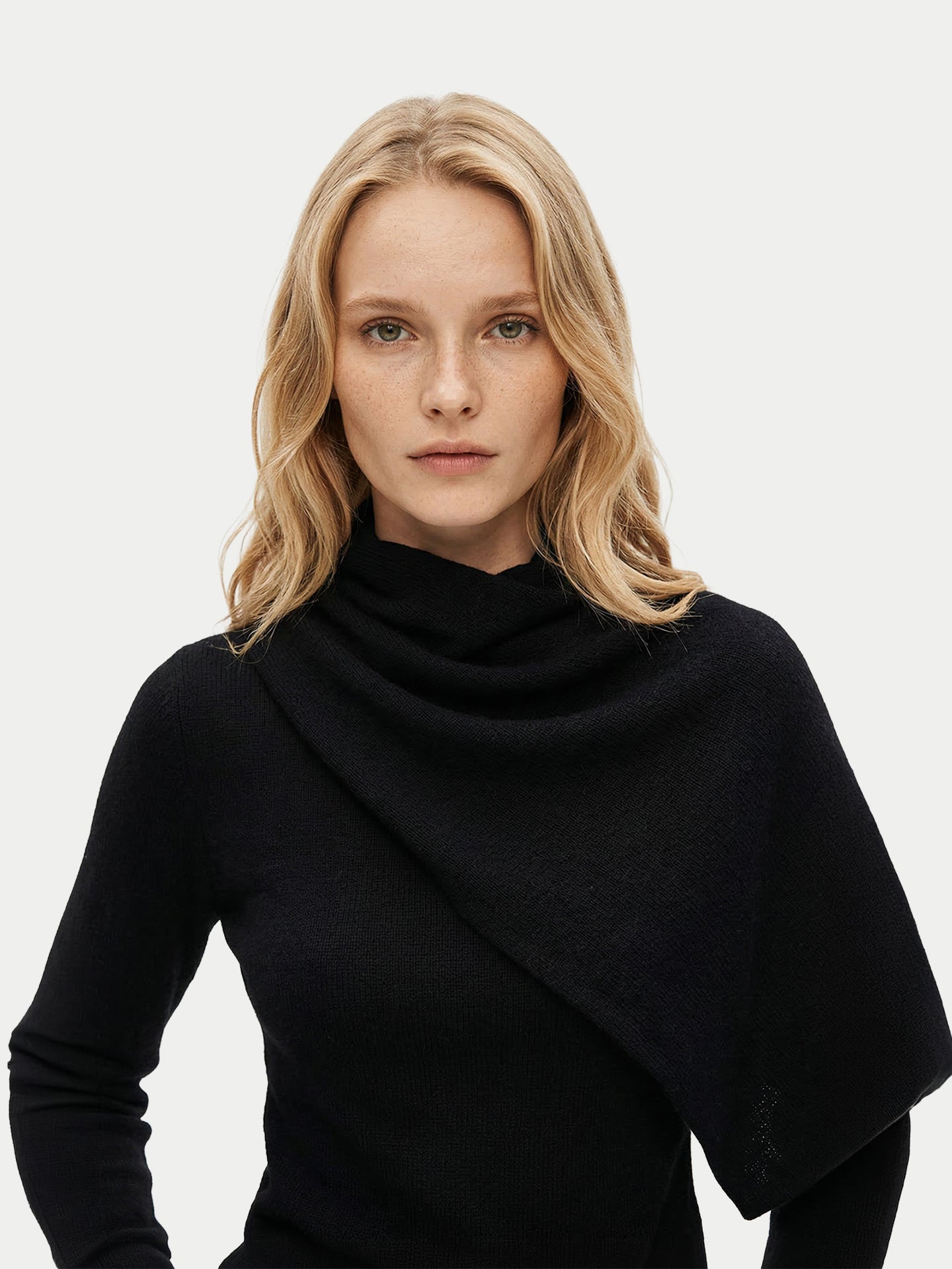 Vue de face d'une femme portant un pull noir à manches longues avec une écharpe intégrée, sur un fond gris clair. #color_noir