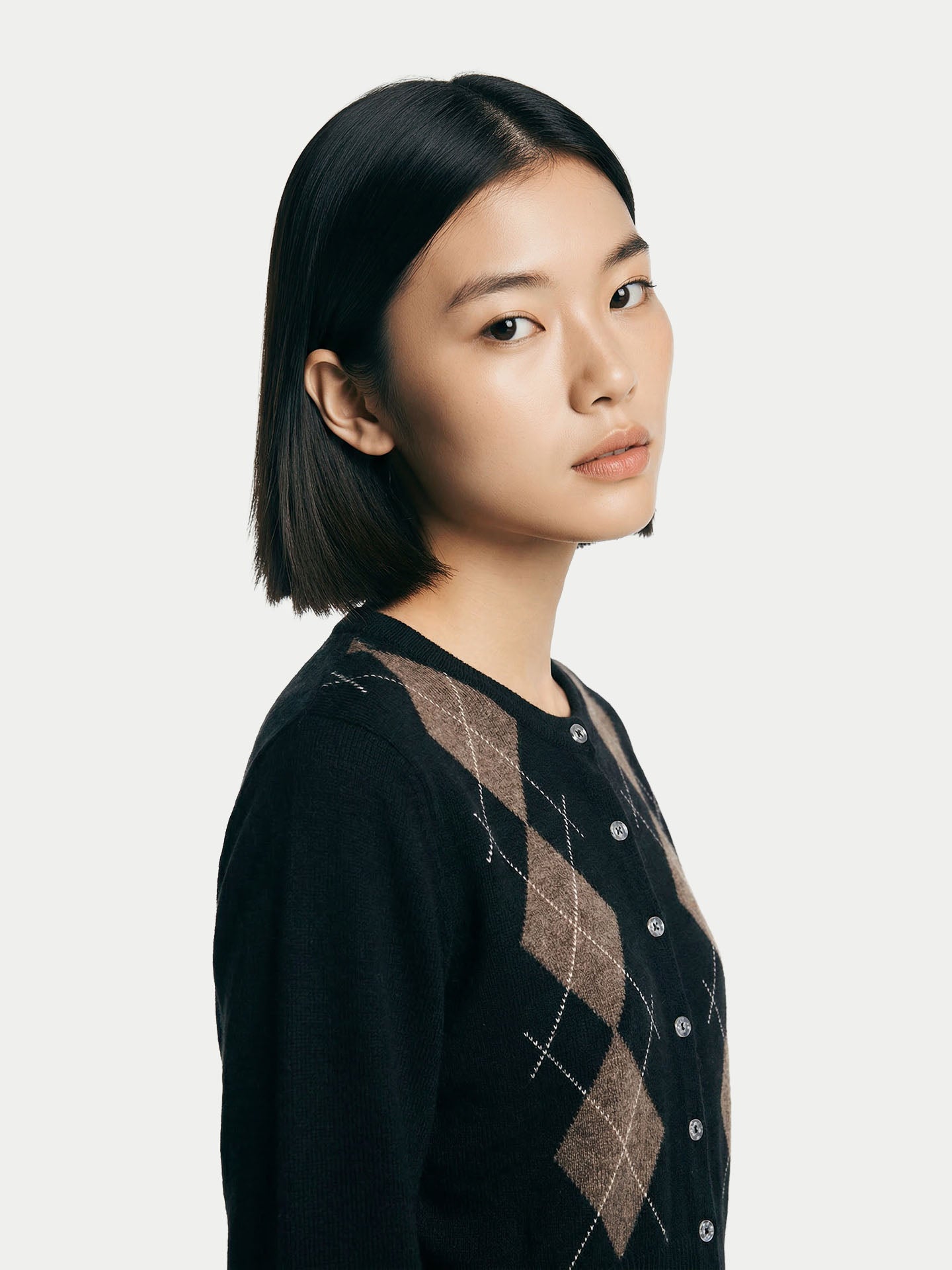 Gros plan de profil d'une femme portant un cardigan noir à col rond et un pantalon assorti à motif losanges marron, sur fond gris clair. #color_noir