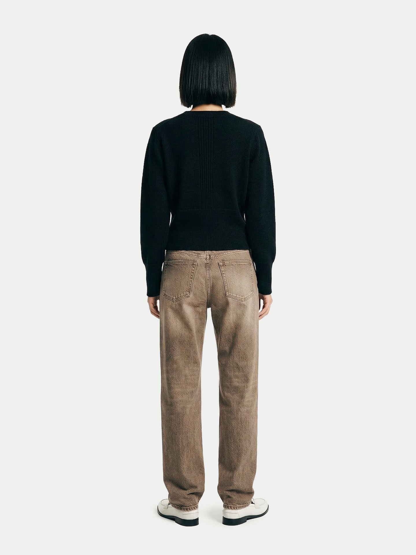 Vue de dos d'une femme portant un cardigan noir, un jean marron et des chaussures blanches sur un fond gris clair. #color_noir