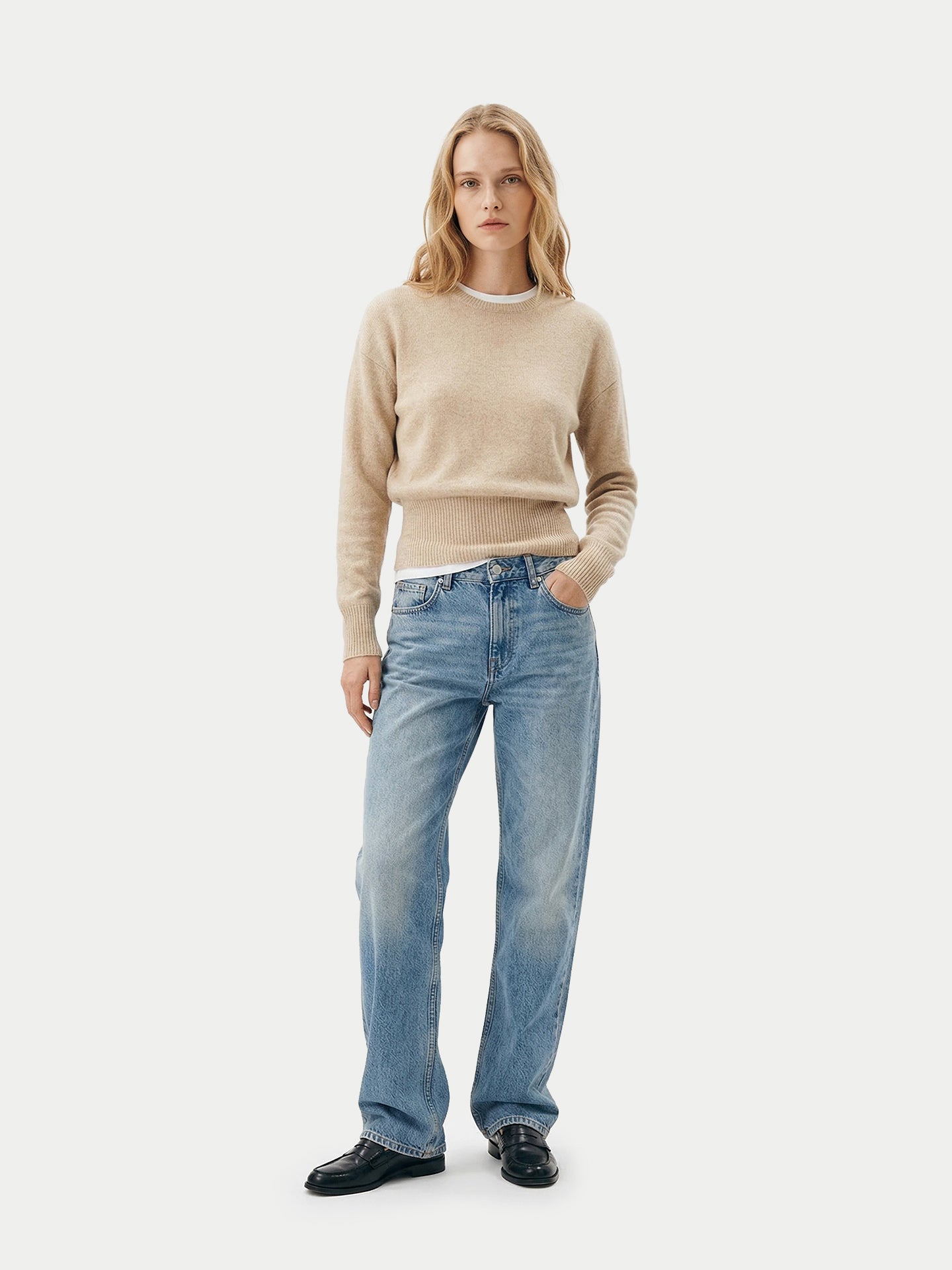 Vue de face d'un pull beige à manches longues, poignets et taille côtelés, porté sur une chemise blanche, un jean bleu et des mocassins noirs sur un fond gris clair. #color_beige