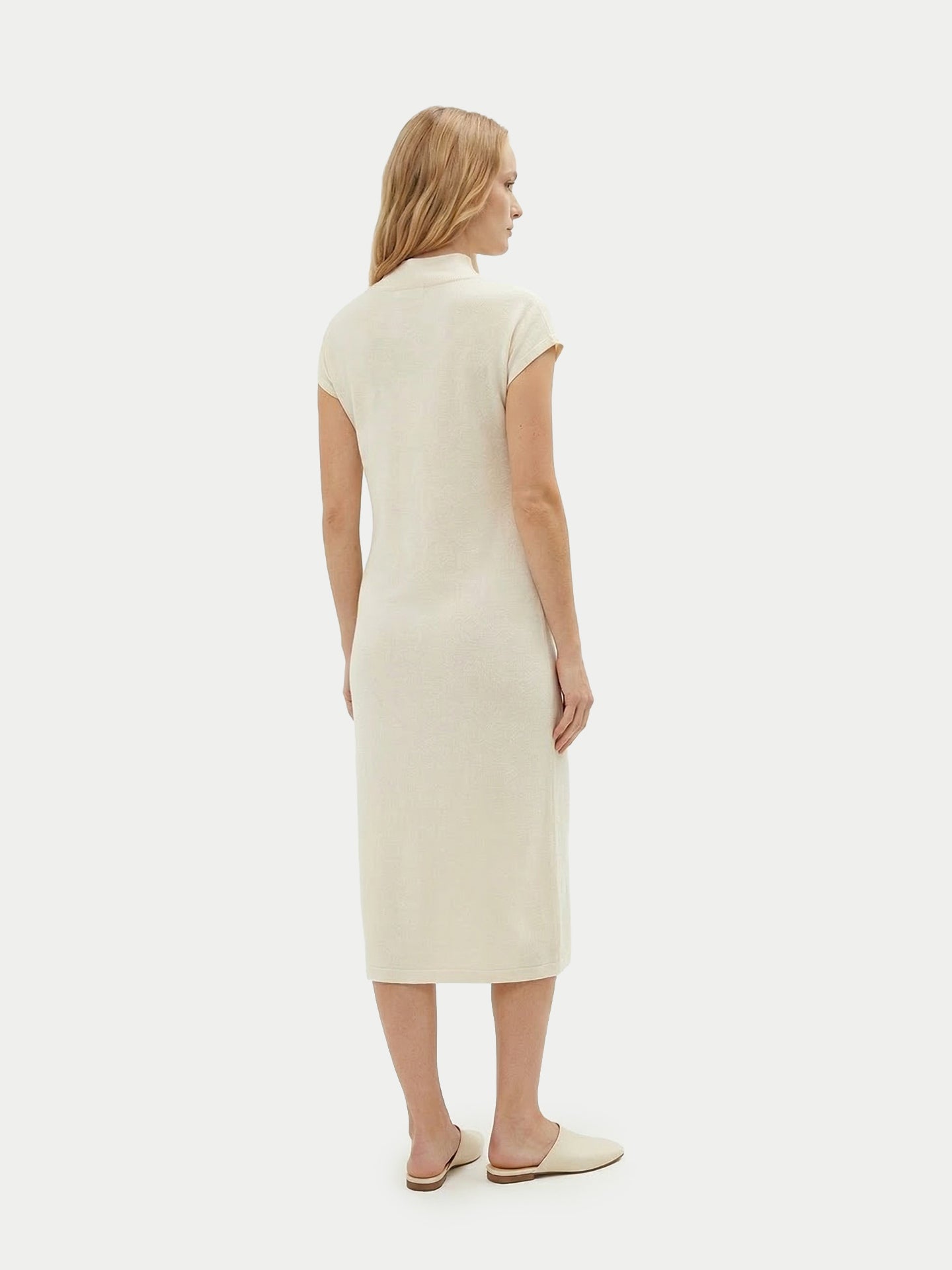 Vue de dos d'une femme portant une robe blanche à manches courtes arrivant sous le genou, avec un foulard noué, sur un fond gris clair. #color_blanc