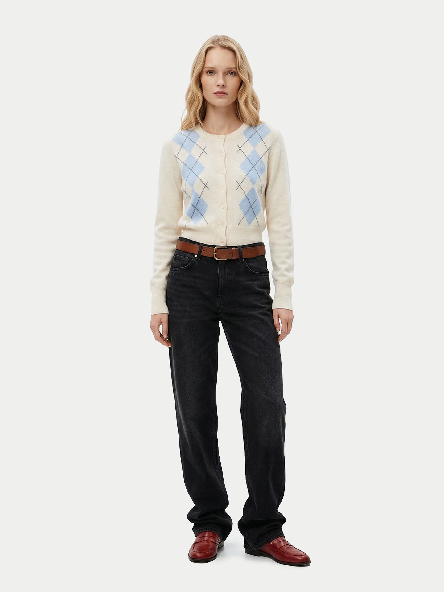 Vue de face d'une femme portant un cardigan blanc à col rond, à motifs losanges bleu clair, avec poignets et taille côtelés, un jean noir et des mocassins marron sur fond gris clair. #color_blanc