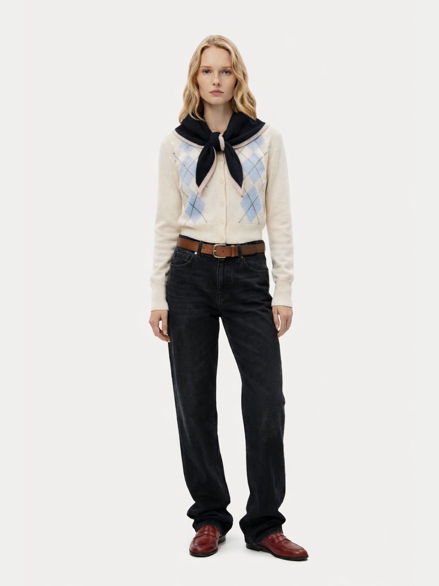 Vue de face d'une femme portant un pull à motifs, une écharpe noire nouée sur l'épaule et un pantalon noir sur fond blanc. #color_noir