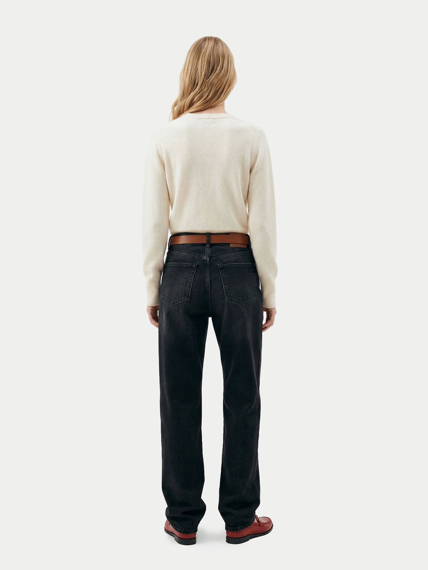 Vue de dos d'une femme portant un cardigan blanc, un jean noir avec une ceinture marron et des mocassins sur un fond gris clair.#color_blanc