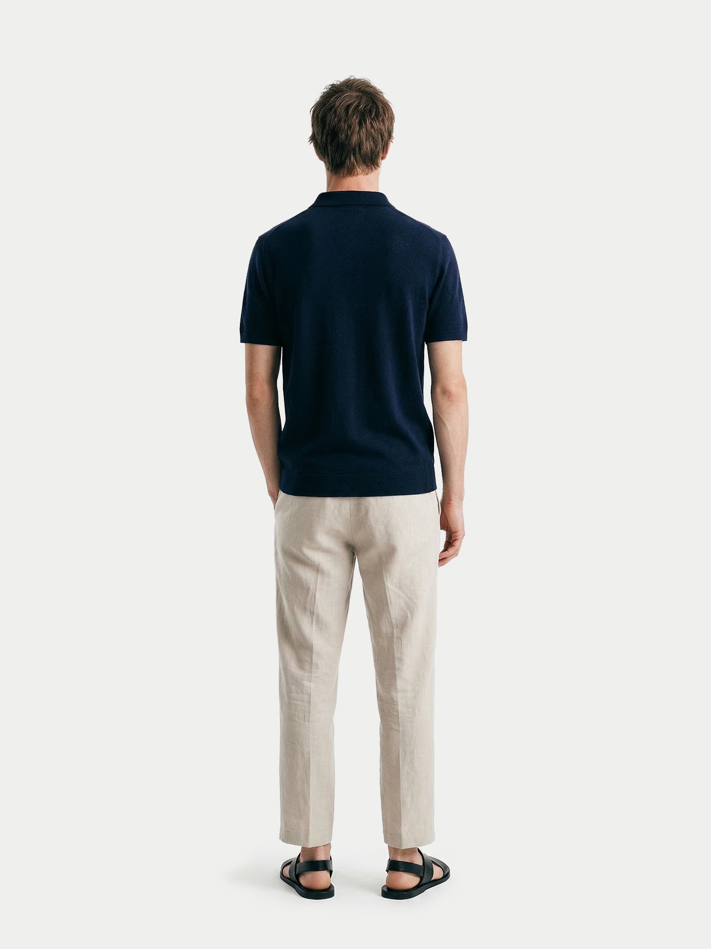 Vue de dos d'un homme portant un t-shirt en cachemire bleu marine à col et demi-zip et un pantalon beige sur fond gris clair. #color_mood-indigo