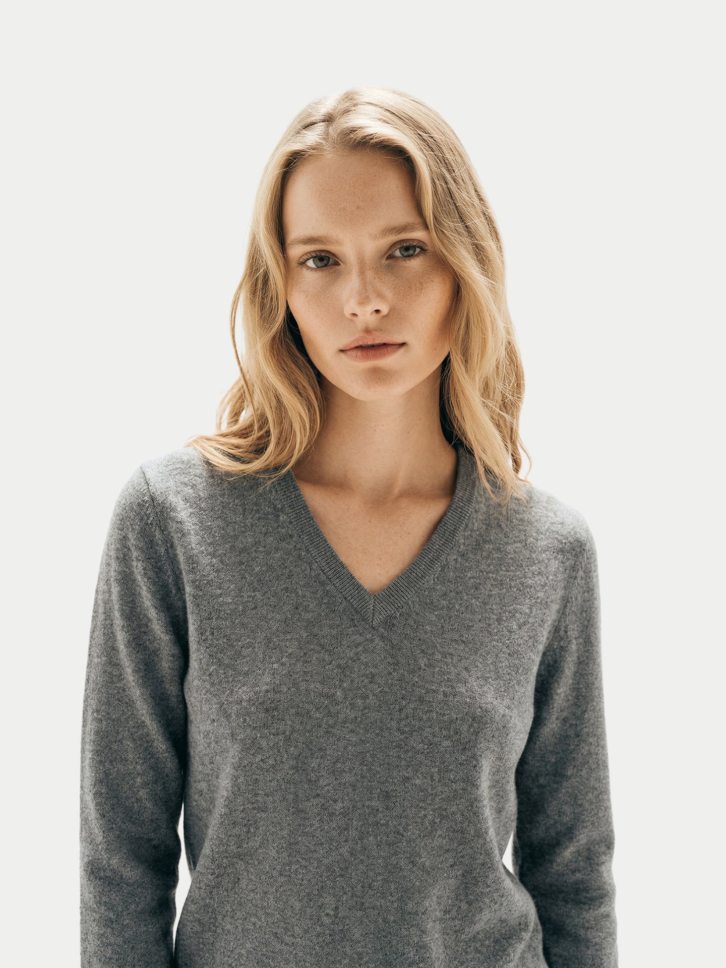 Gros plan de face d'une femme portant un pull gris foncé à col en V sur fond gris clair. #color_gris-foncé