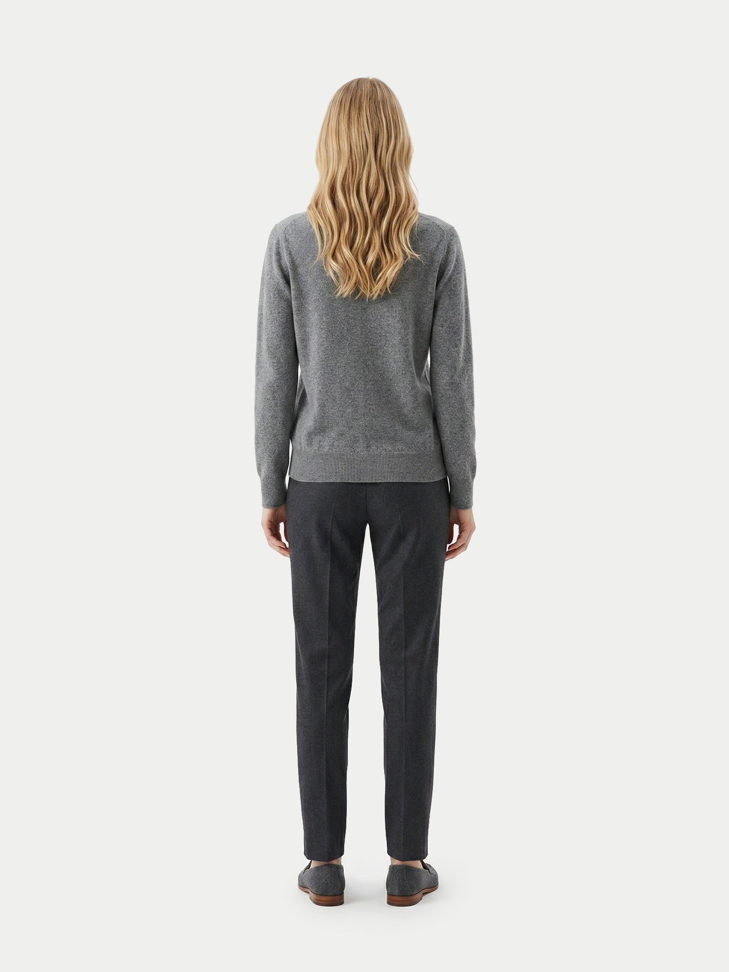 Vue de dos d'une femme portant un pull gris foncé, un pantalon noir et des mocassins sur un fond gris clair. #color_gris-foncé