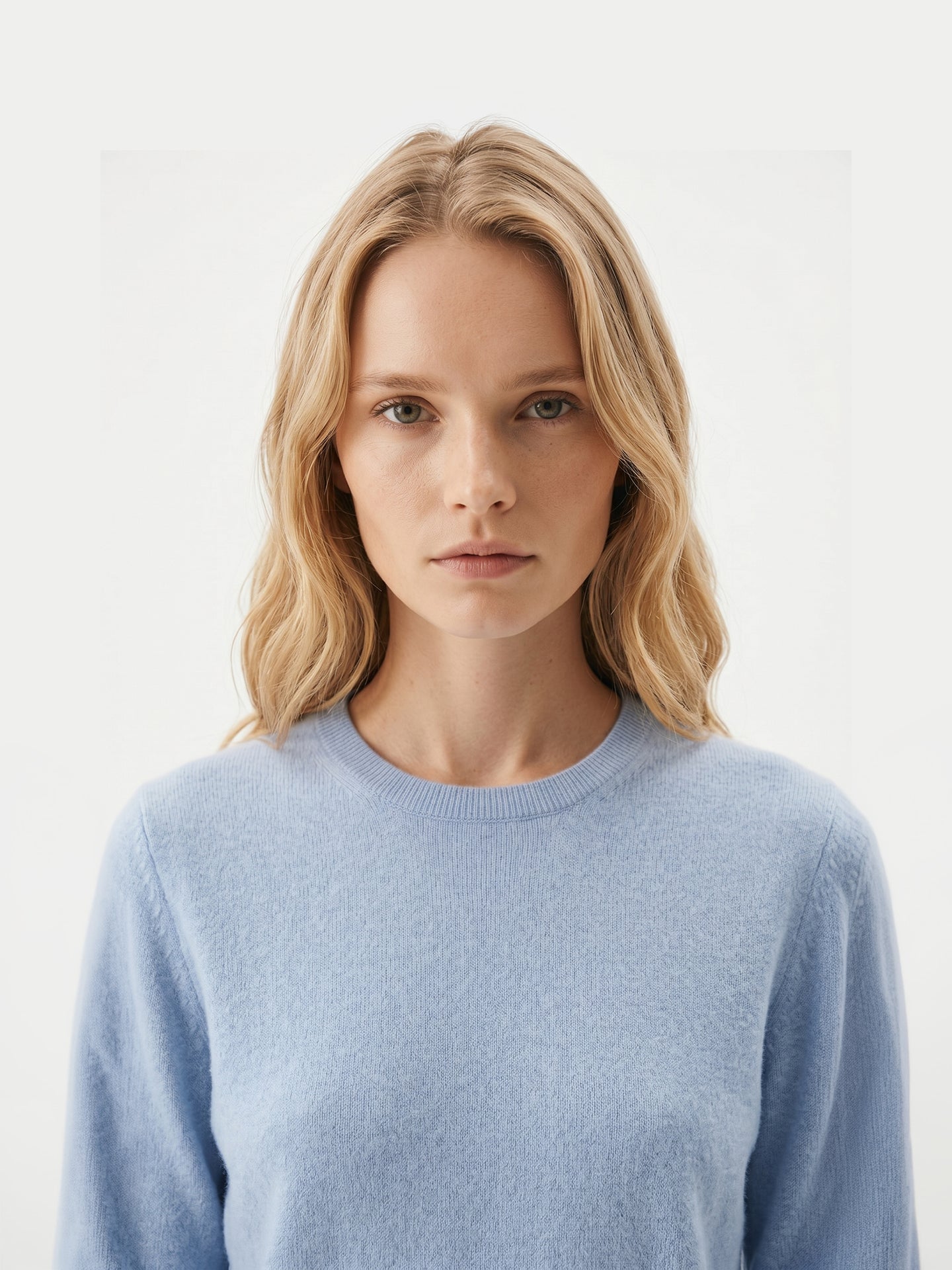 Gros plan de face d'une femme portant un pull ras du cou bleu clair sur fond gris clair. #color_bleu-clair