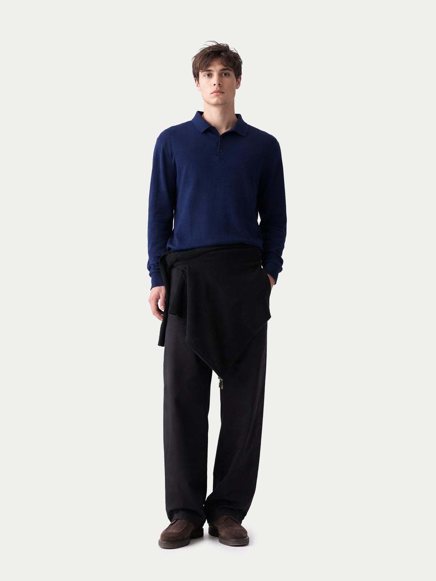 Vue de face d'un homme portant un polo bleu marine à manches longues et un pantalon noir sur fond gris clair. #color_mood-indigo