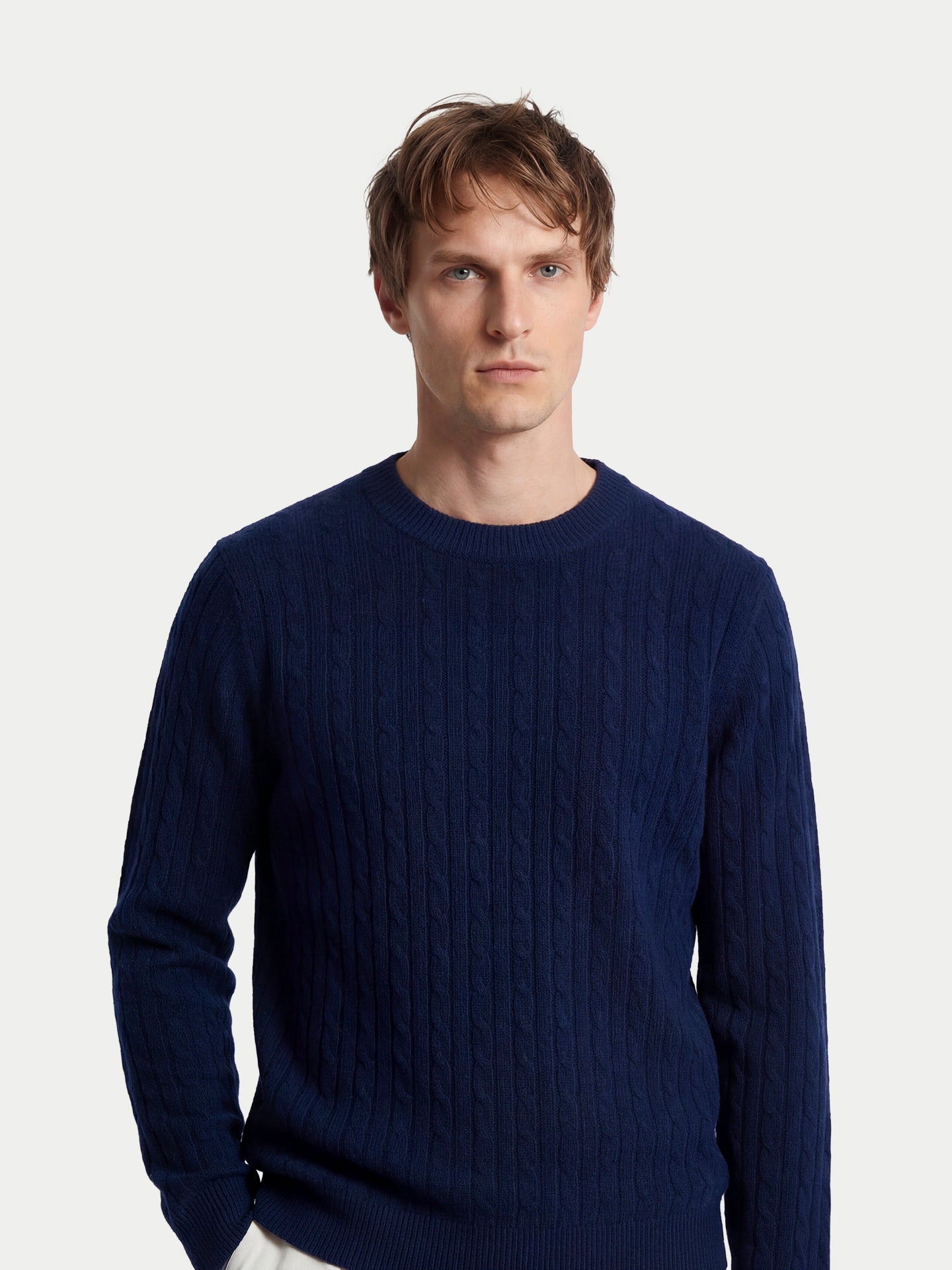 Gros plan de face d'un homme debout portant un pull en cachemire à col rond bleu marine sur fond gris clair. #color_navy