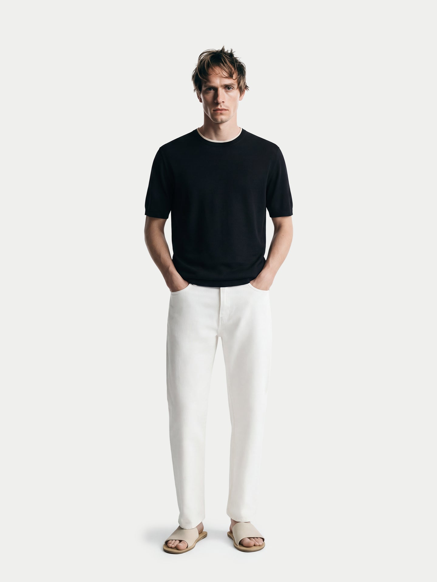 Vue de face d'un homme portant un t-shirt en cachemire noir à col rond blanc et un pantalon blanc sur fond gris clair. #color_noir