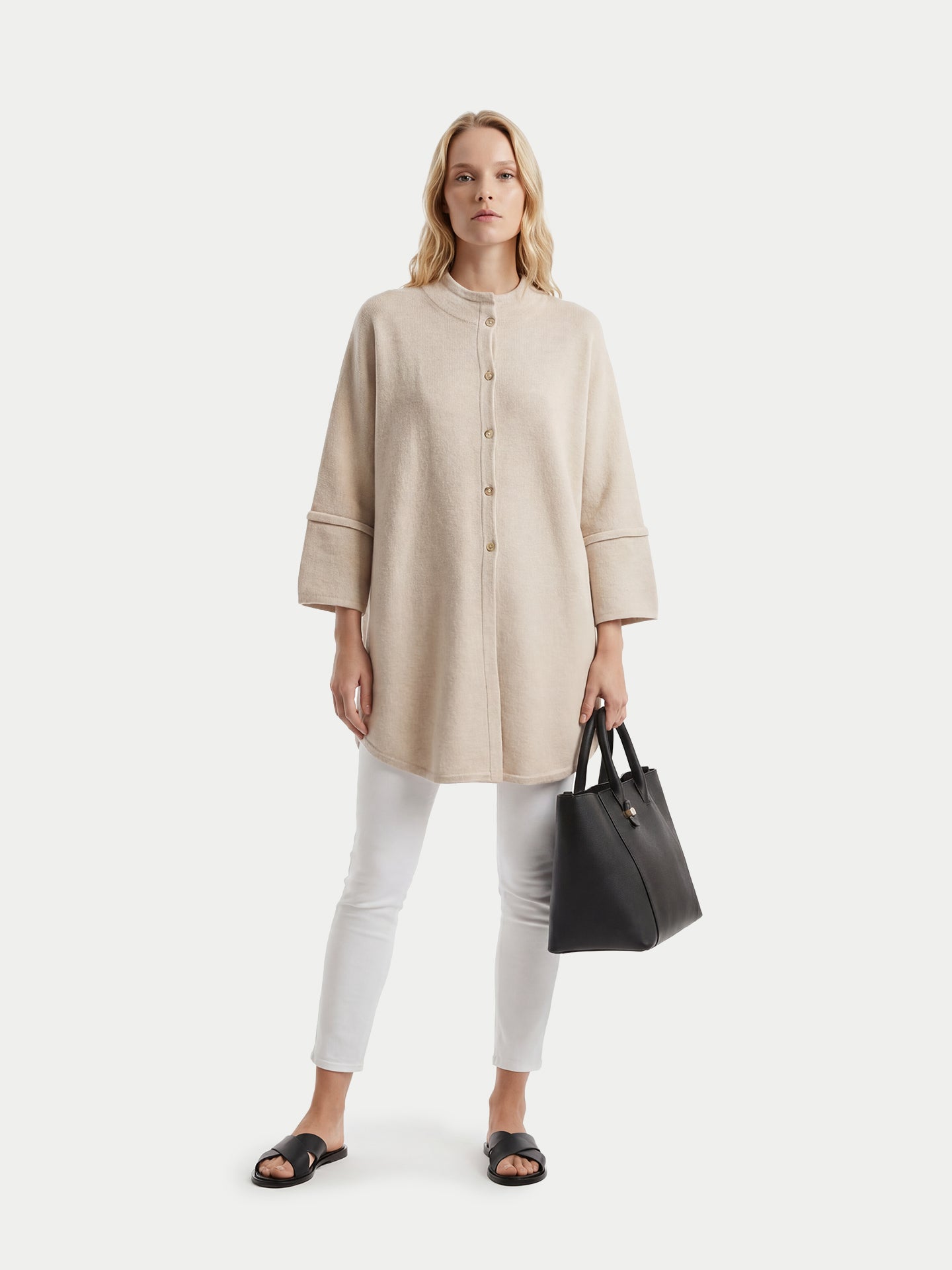 Femme portant un poncho beige à boutons et tenant un sac à main noir sur fond blanc #color_beige