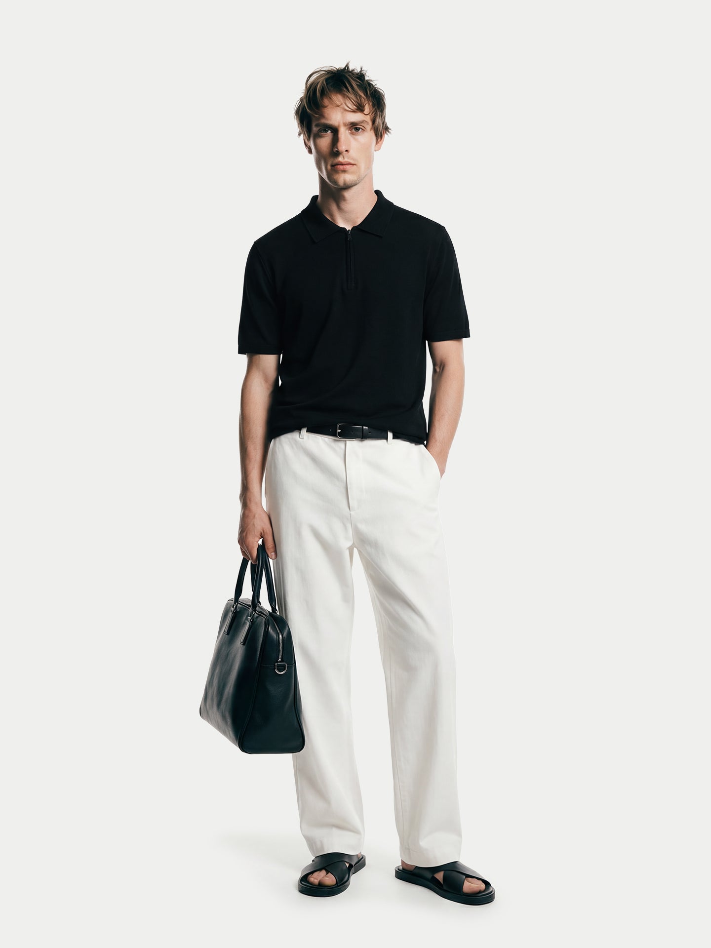 Vue de face d'un homme portant un t-shirt noir en cachemire à col et demi-zip et un pantalon blanc sur fond gris clair. #color_noir