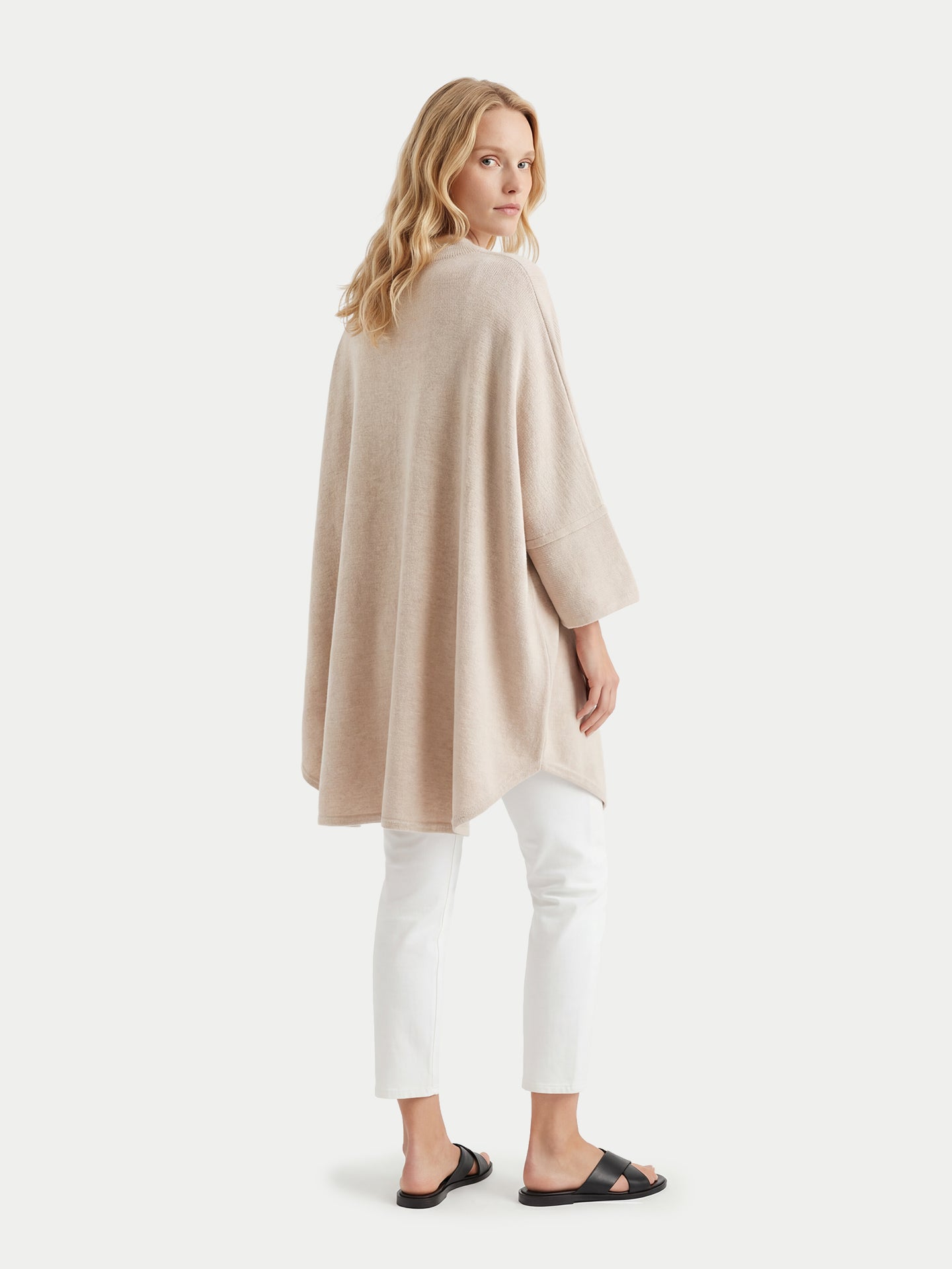 Vue de dos d'une femme portant un poncho beige et un legging blanc sur fond blanc #color_beige