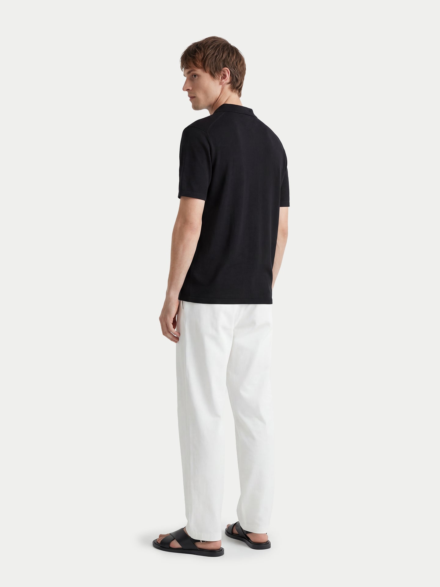 Vue de dos d'un homme portant un t-shirt en cachemire noir à col et un pantalon blanc sur fond gris clair. #color_noir