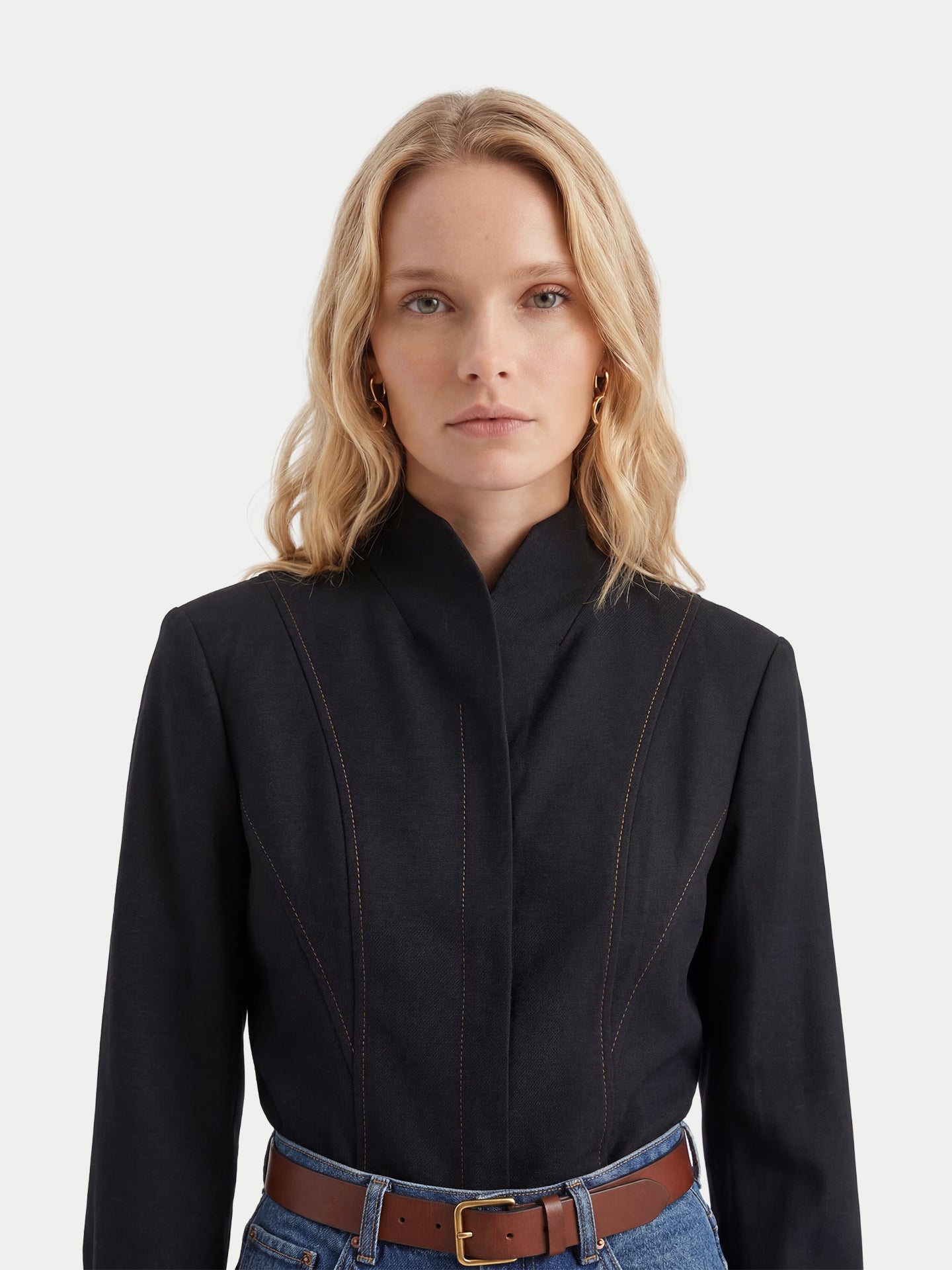 Gros plan sur une femme portant une chemise traditionnelle mongole noire à col en V et manches longues, et un jean bleu, sur fond gris clair. #color_noir