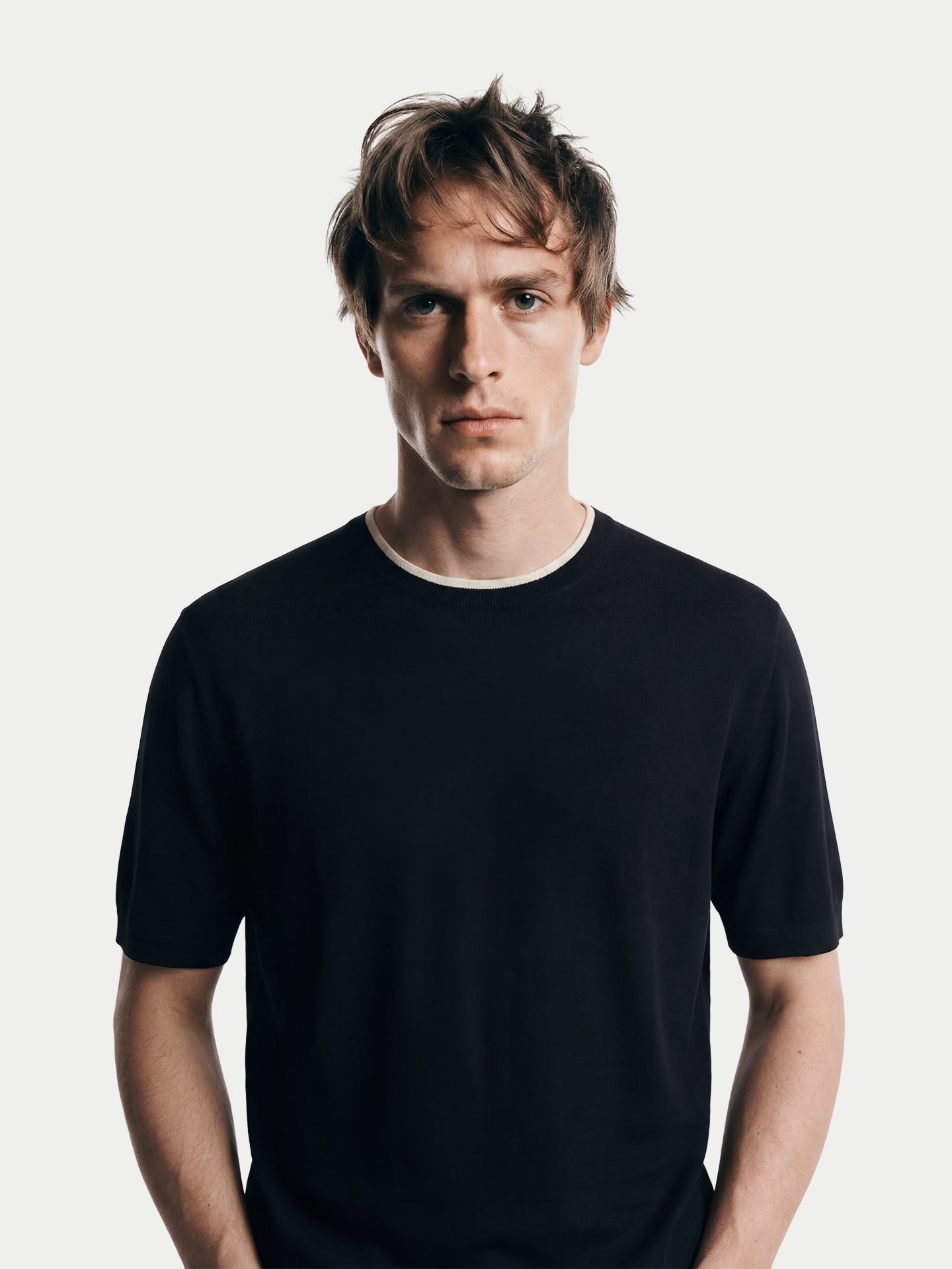 Gros plan de face d'un homme portant un t-shirt en cachemire noir à col rond blanc sur fond gris clair. #color_noir