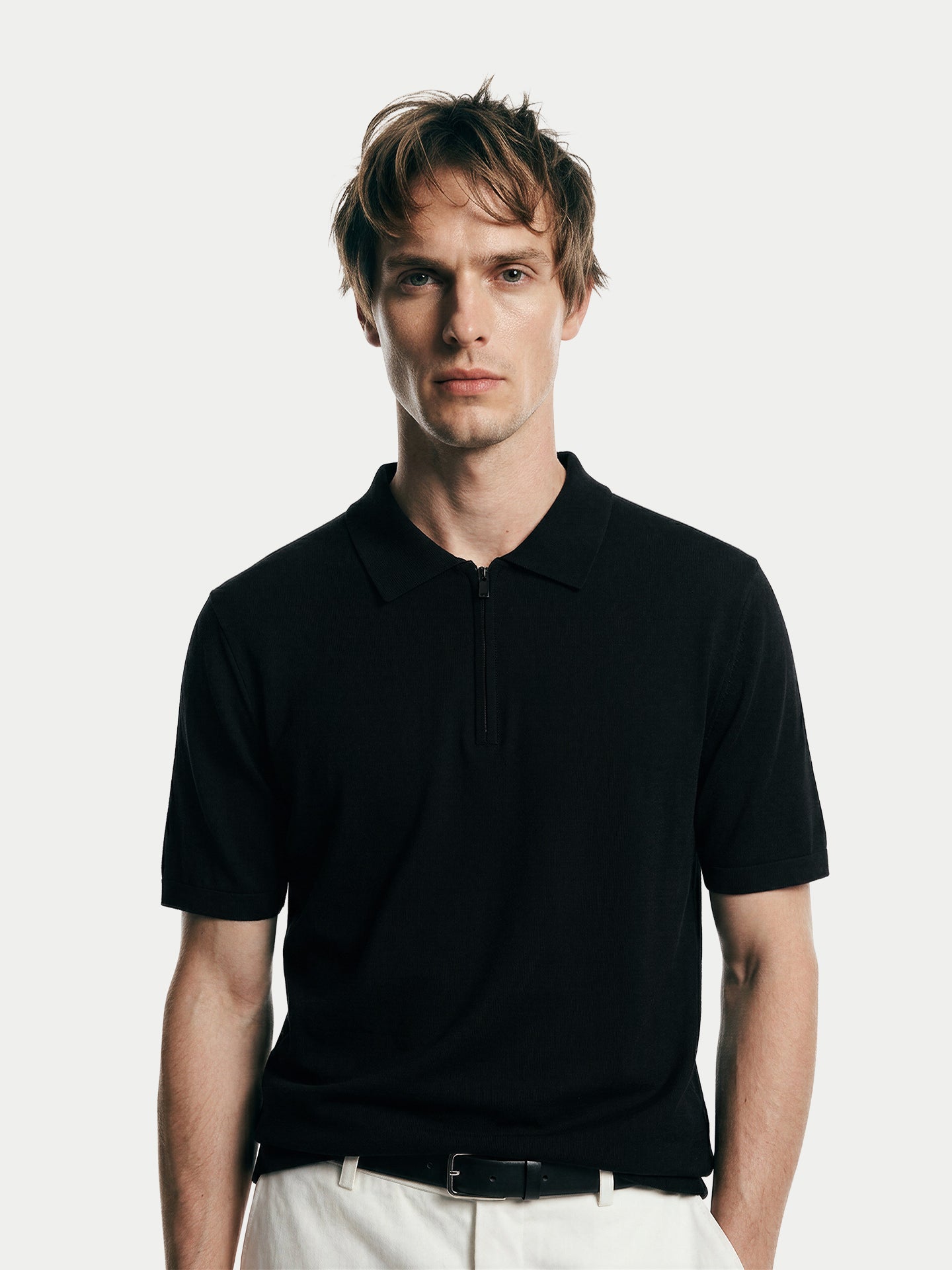 Gros plan de face d'un homme portant un t-shirt noir en cachemire à col et demi-zip sur fond gris clair. #color_noir