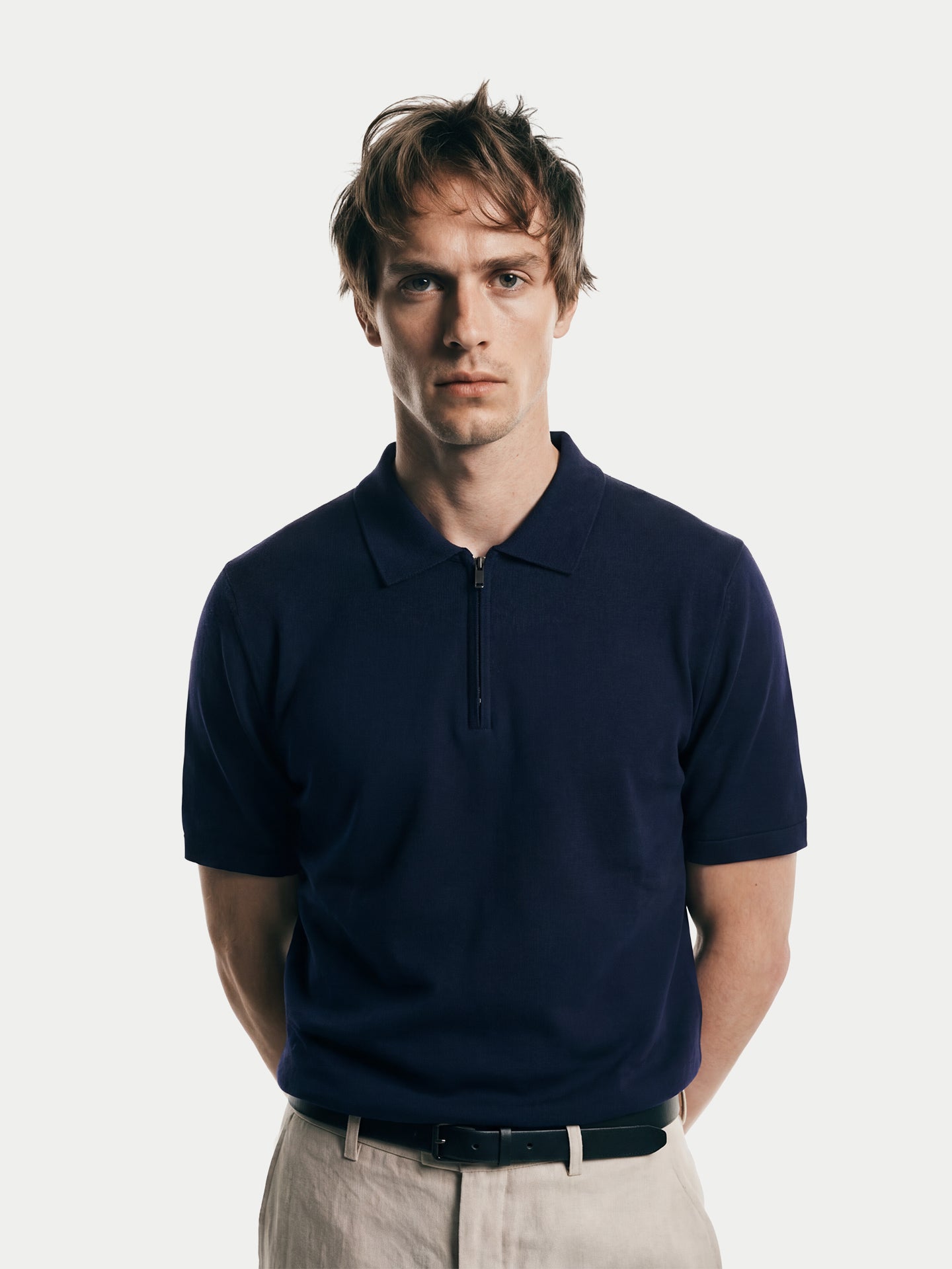 Gros plan de face d'un homme portant un t-shirt en cachemire bleu marine à col et demi-zip sur fond gris clair. #color_mood-indigo