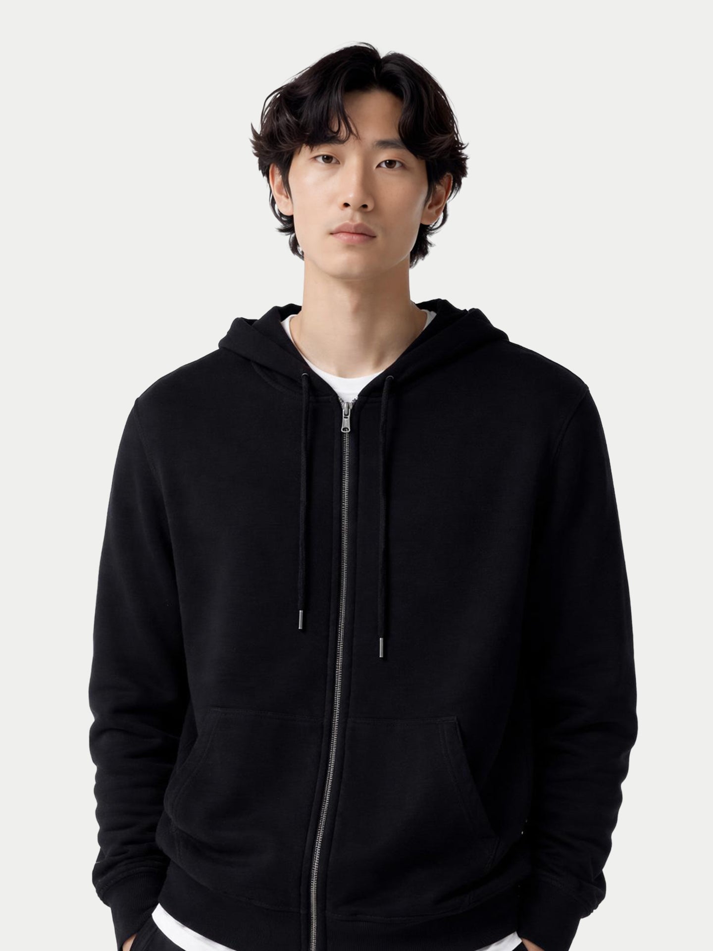 Gros plan de face d'un homme portant un sweat à capuche noir zippé avec poche latérale sur fond gris clair. #color_noir