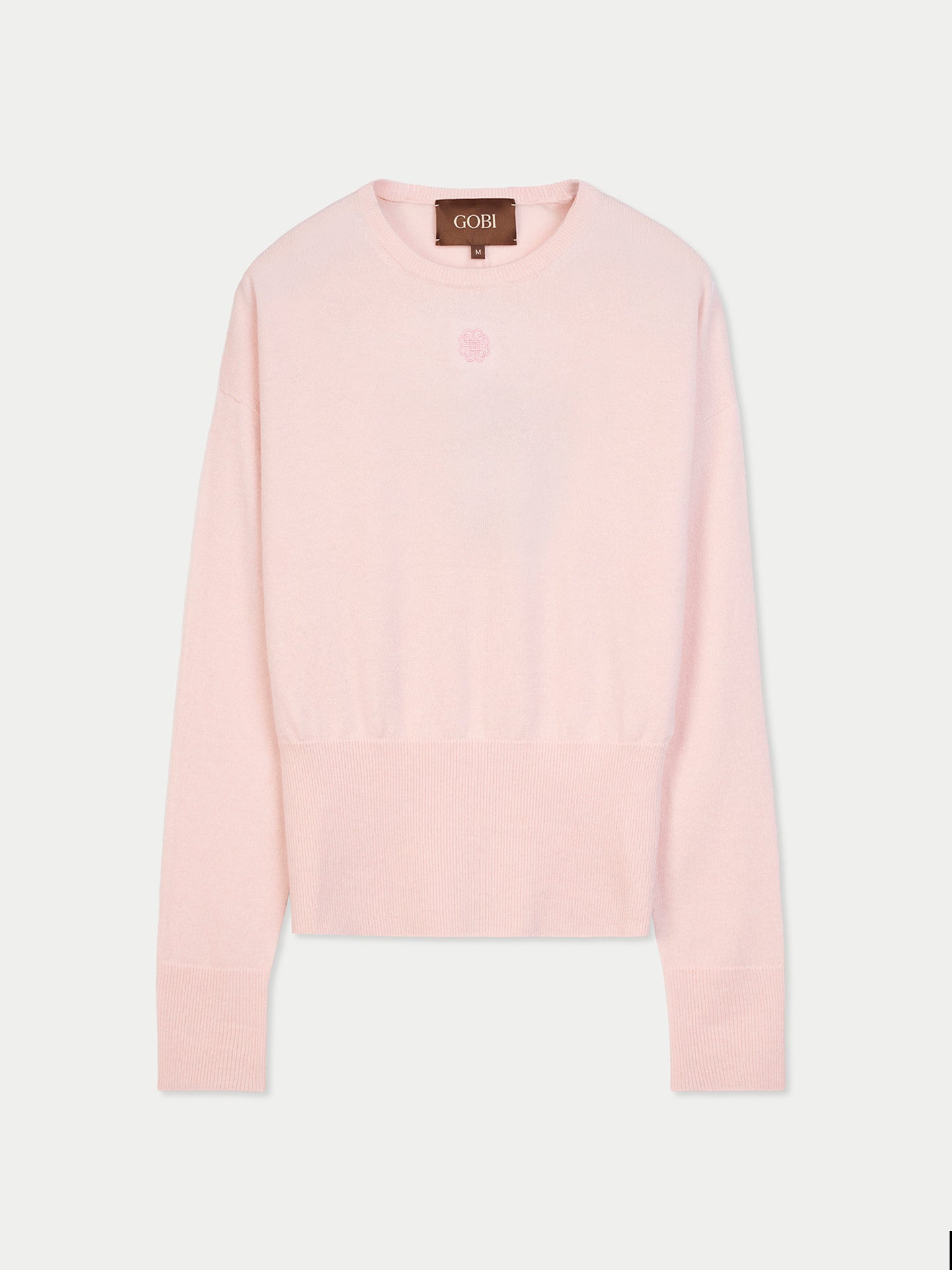 Vue de face d'un pull rose clair à manches longues, avec poignets et taille côtelés et un petit logo de marque en haut sur fond gris clair. #color_peach-blush
