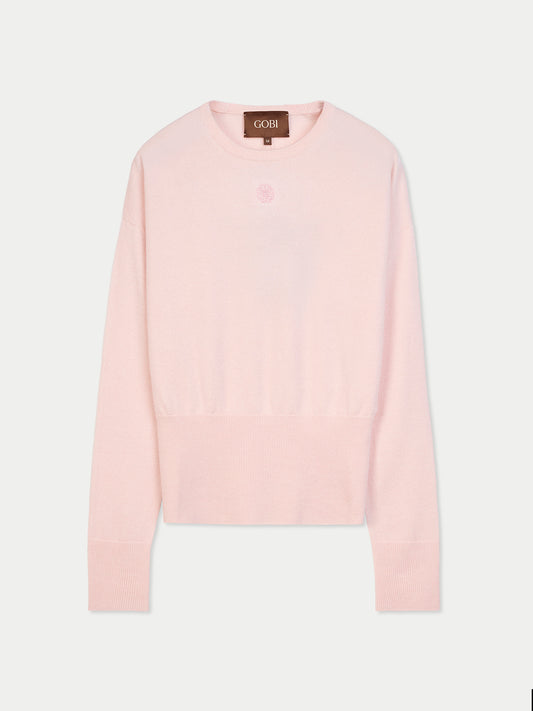 Vue de face d'un pull rose clair à manches longues, avec poignets et taille côtelés et un petit logo de marque en haut sur fond gris clair. #color_peach-blush