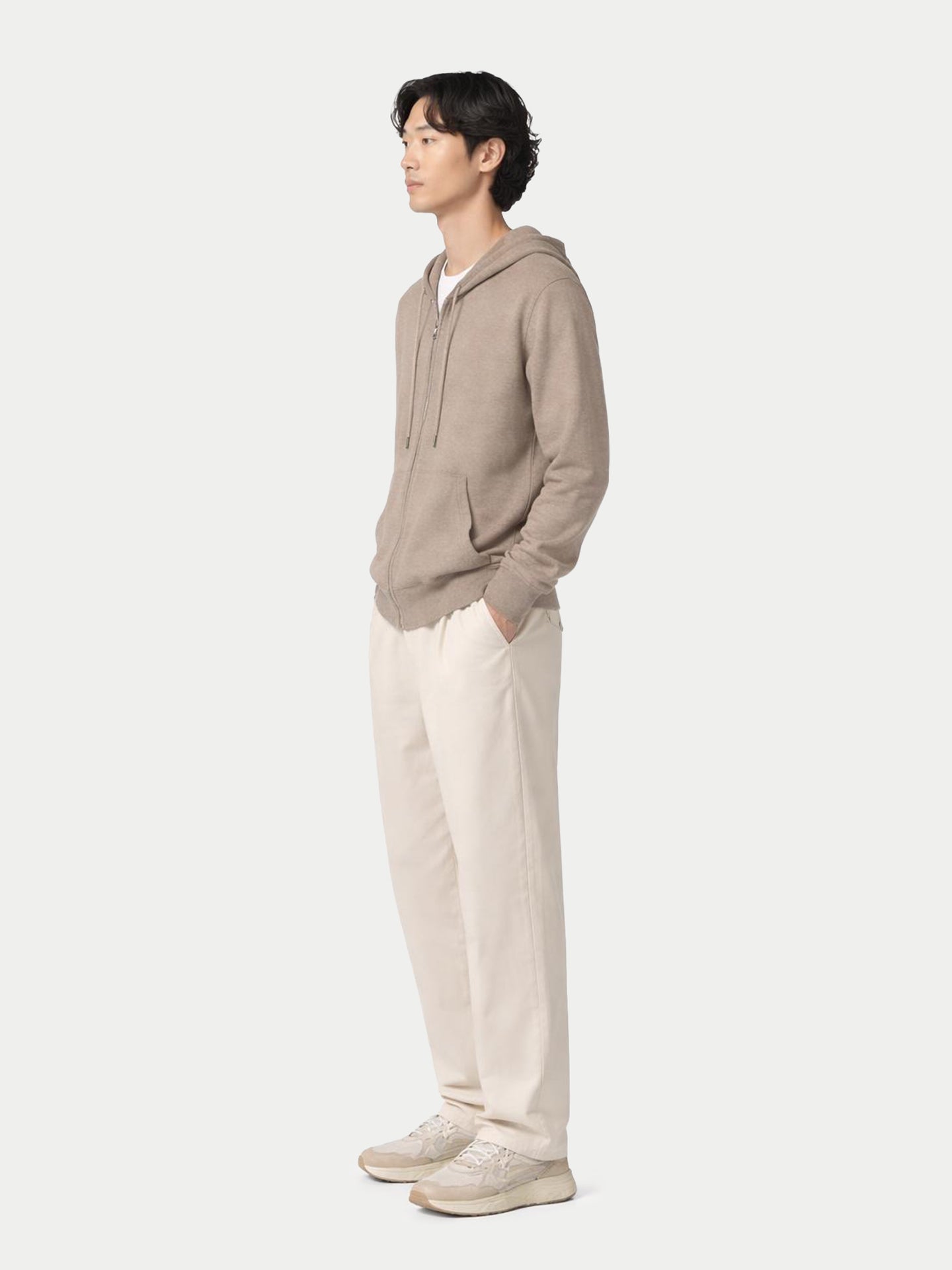Vue de profil d'un homme portant un sweat à capuche beige sur un t-shirt blanc et un pantalon blanc, sur fond gris clair. #couleur_beige