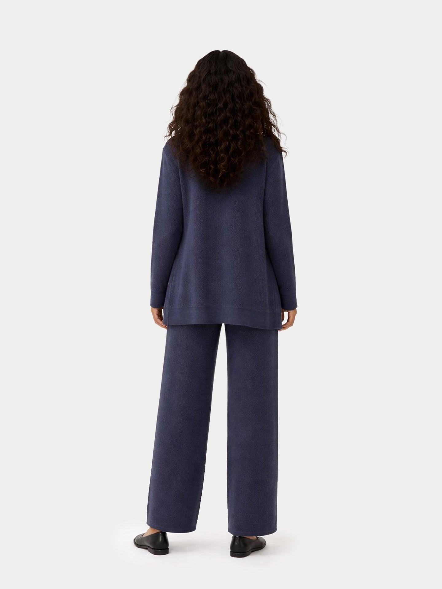 Vue de dos d'une femme portant un cardigan bleu ouvert et un pantalon large en maille côtelée assorti, sur fond gris clair. #color_bleu-courrone